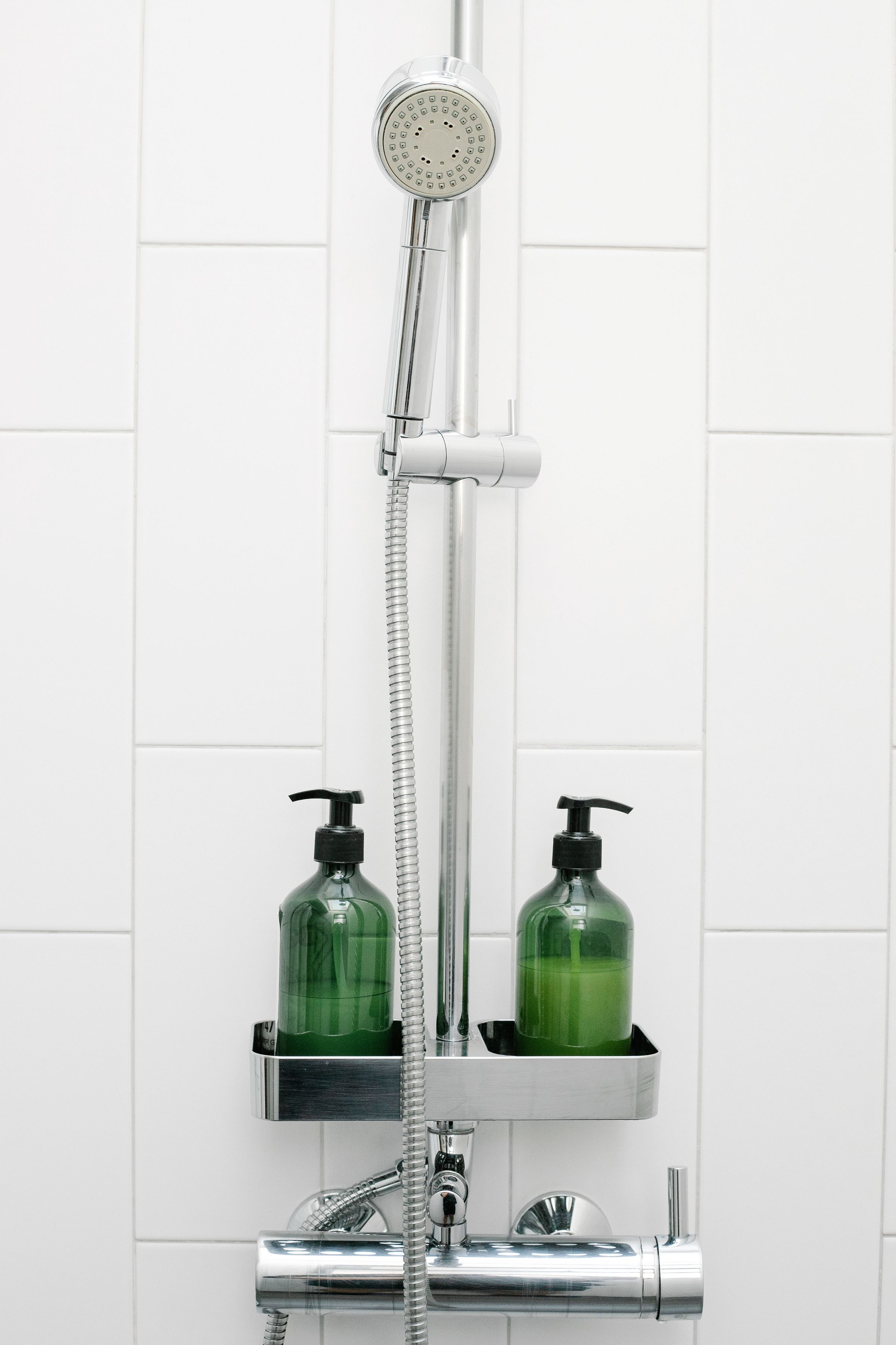Two pump bottles beside a shower hose against white tiles.