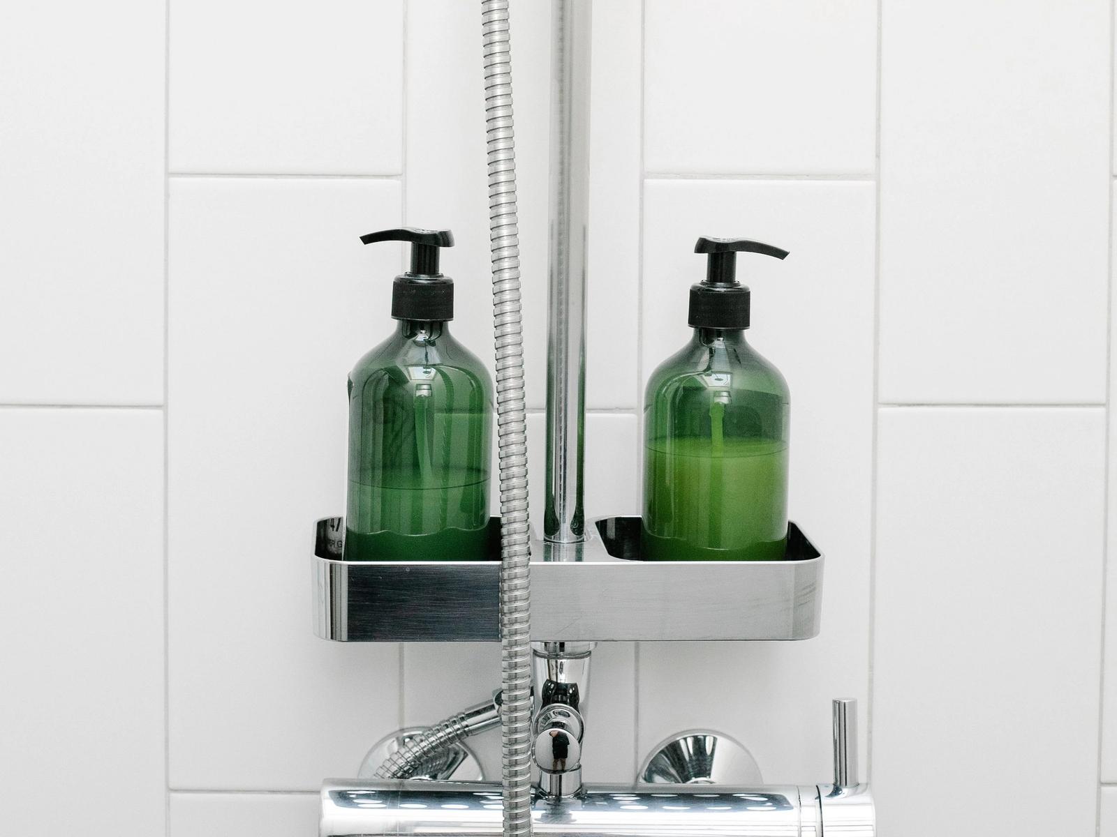 Two pump bottles beside a shower hose against white tiles.