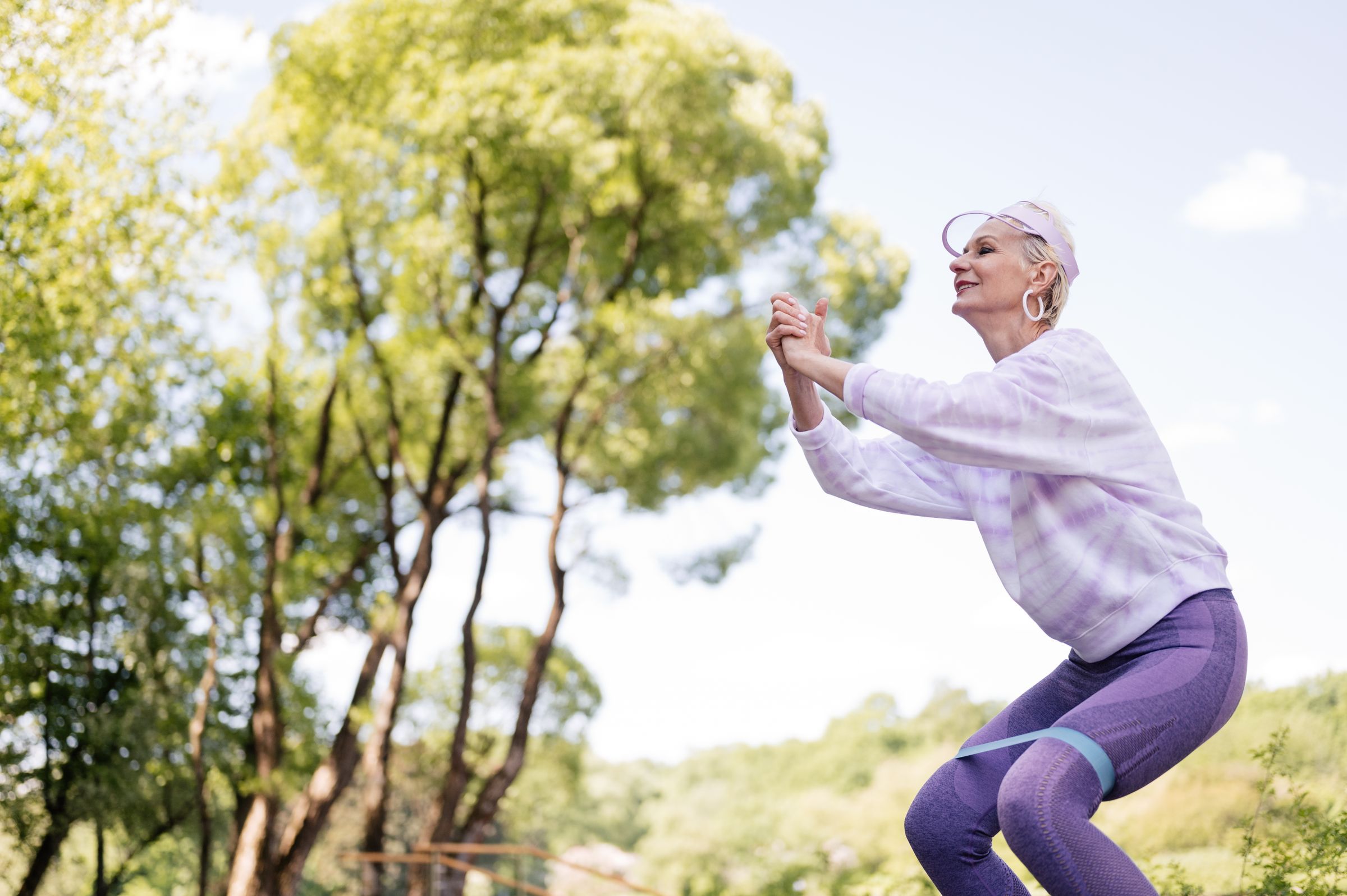 An older woman exercising with a resistance band outdoors.