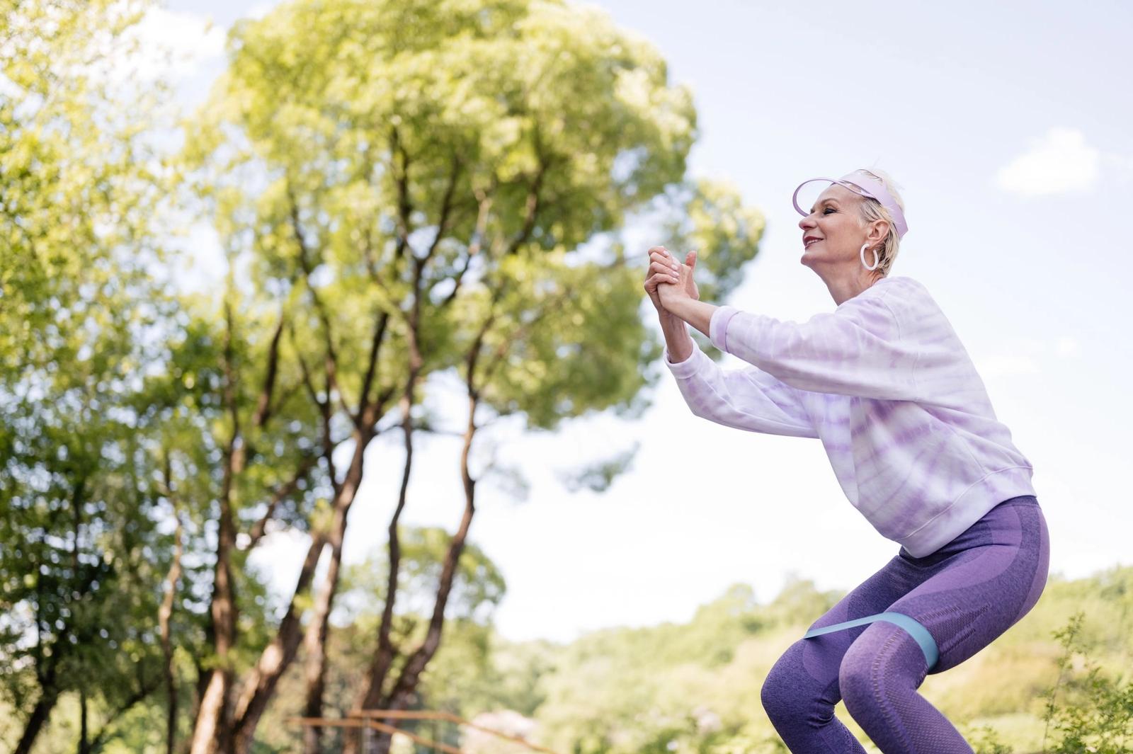 An older woman exercising with a resistance band outdoors.