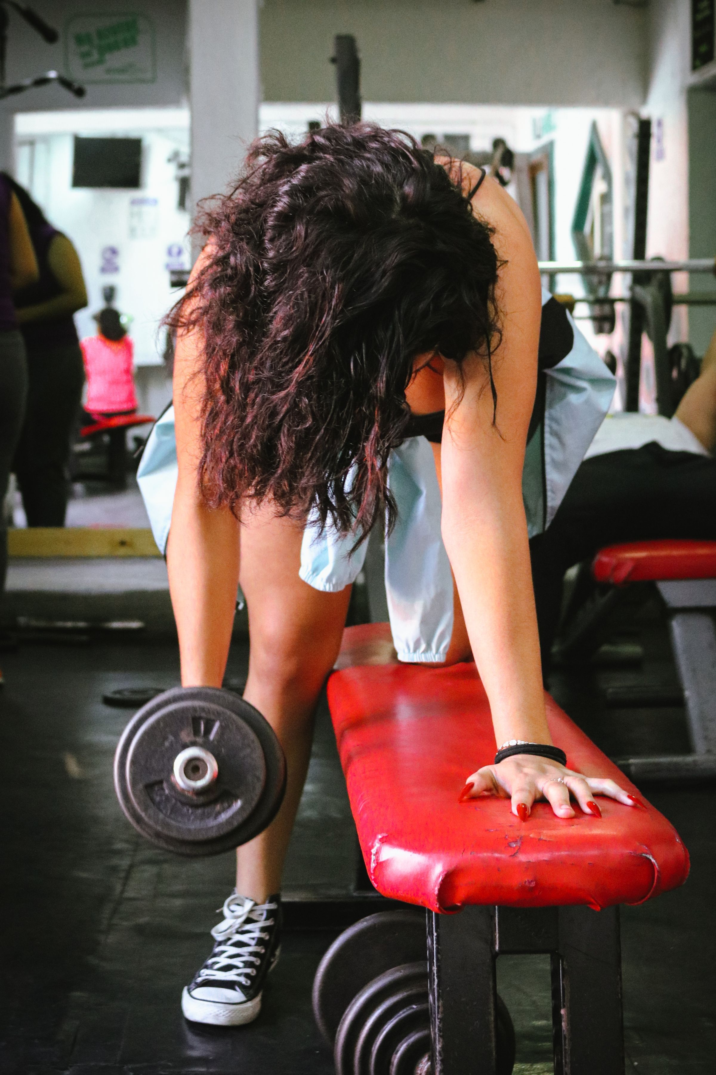 Hands holding a dumbbell and resting on a red gym bench.