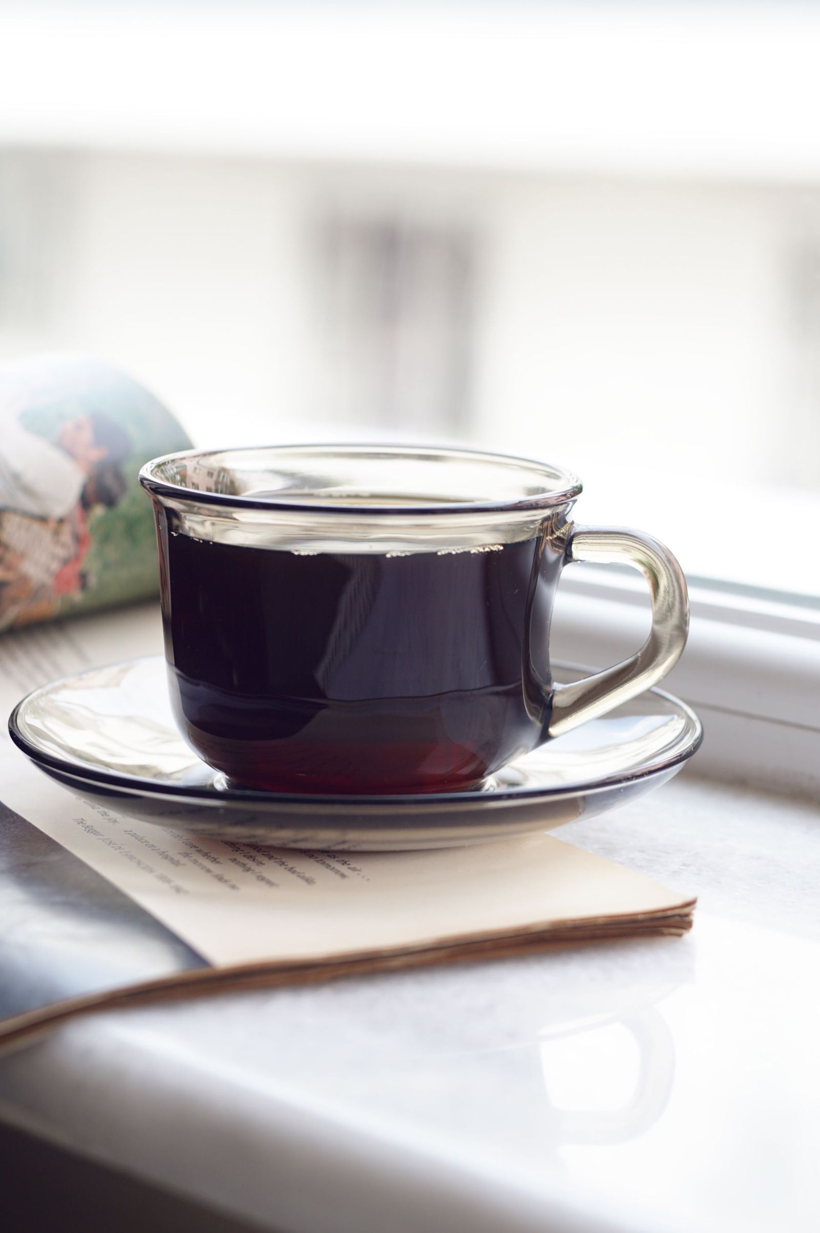 A cup on a saucer above a journal by a window.