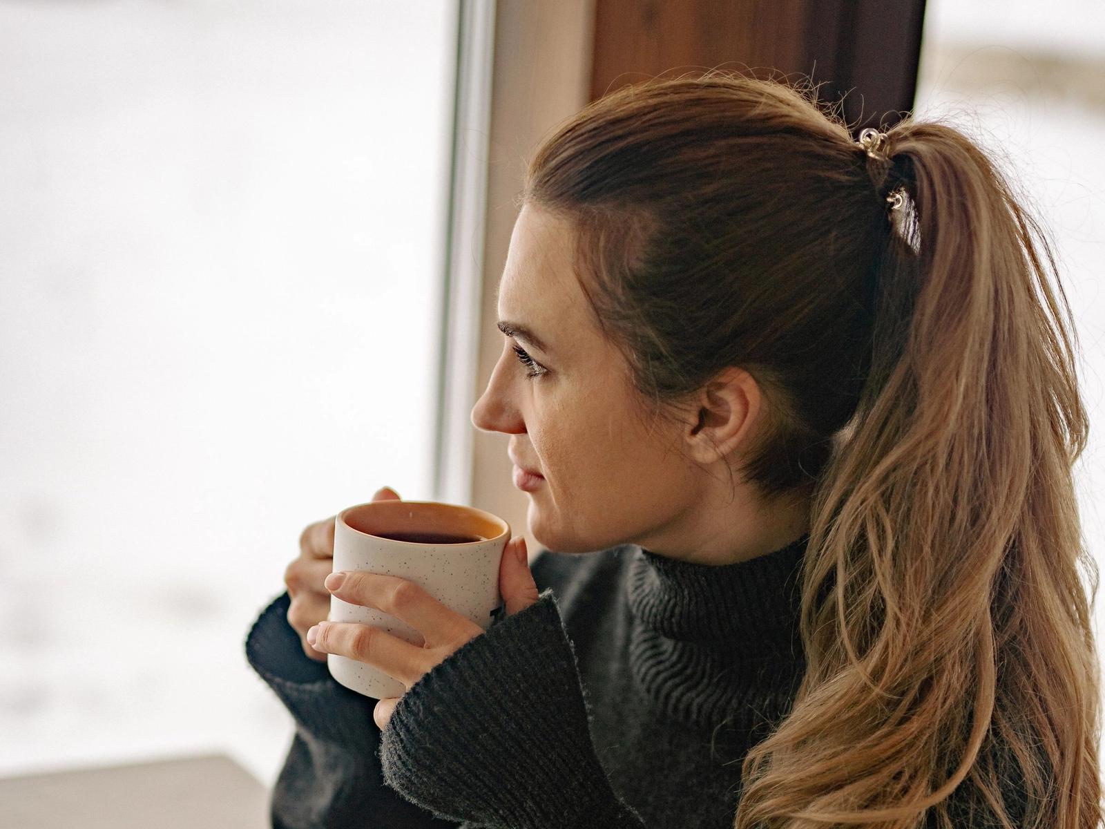 A woman holding a mug beside a window.
