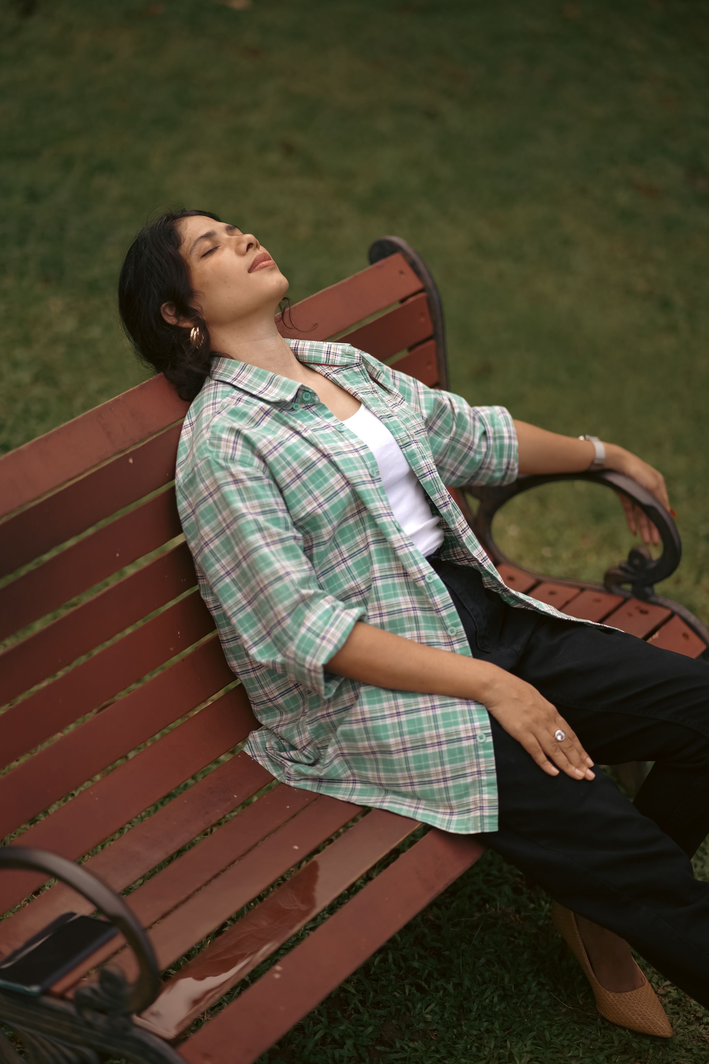 A woman sitting back on a park bench with her eyes closed.