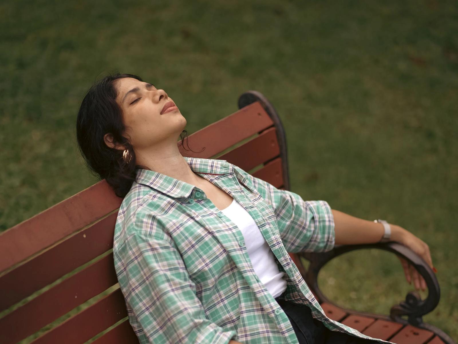 A woman sitting back on a park bench with her eyes closed.