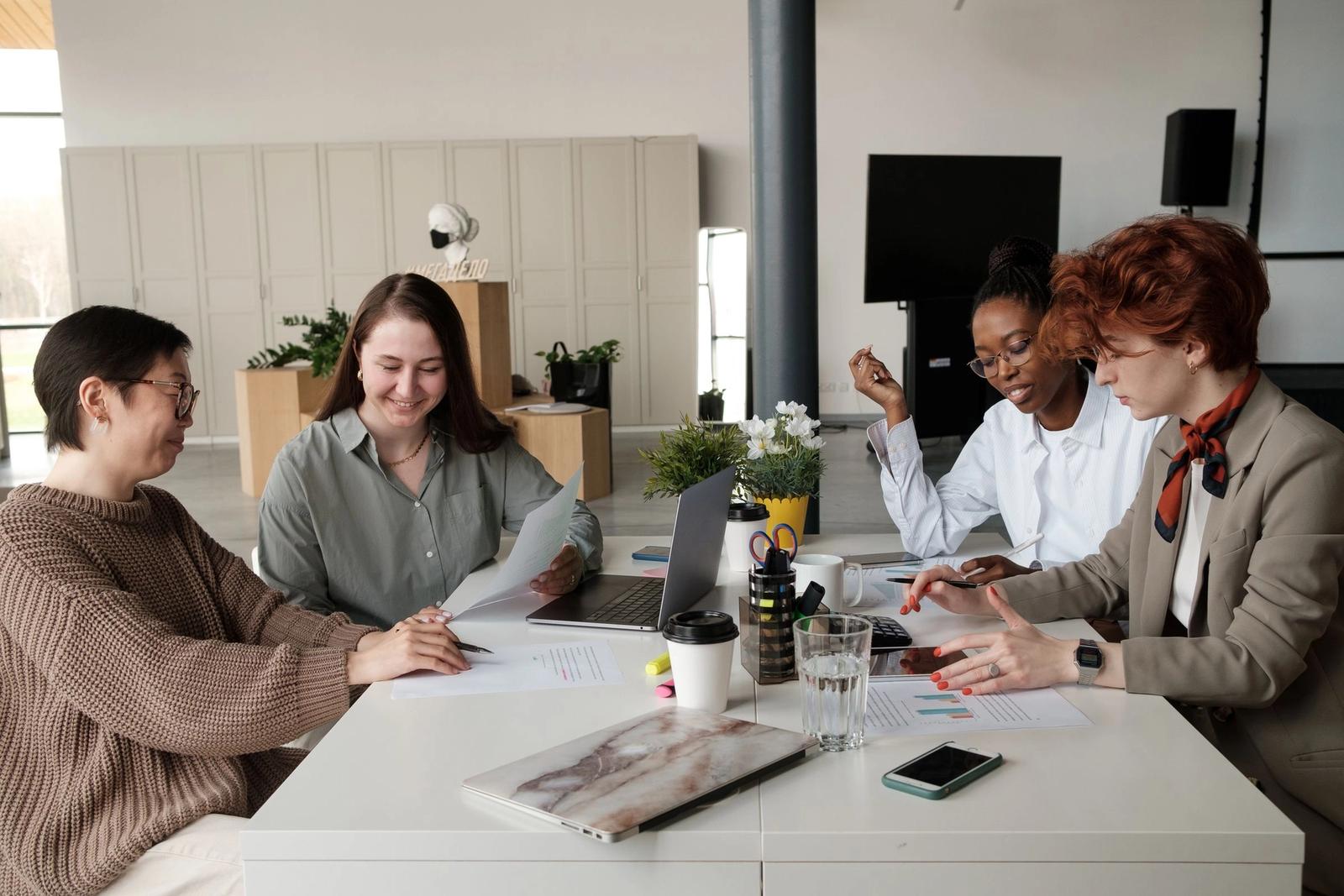 Four women discussing papers around an office table.
