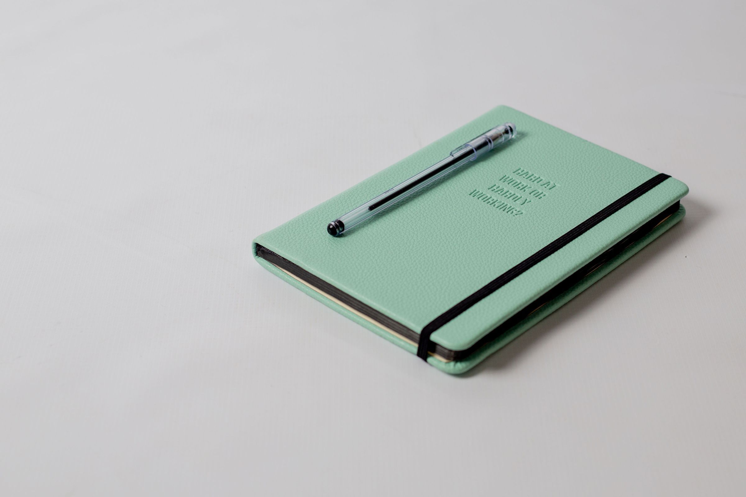 A green notebook and pen on a pale surface.