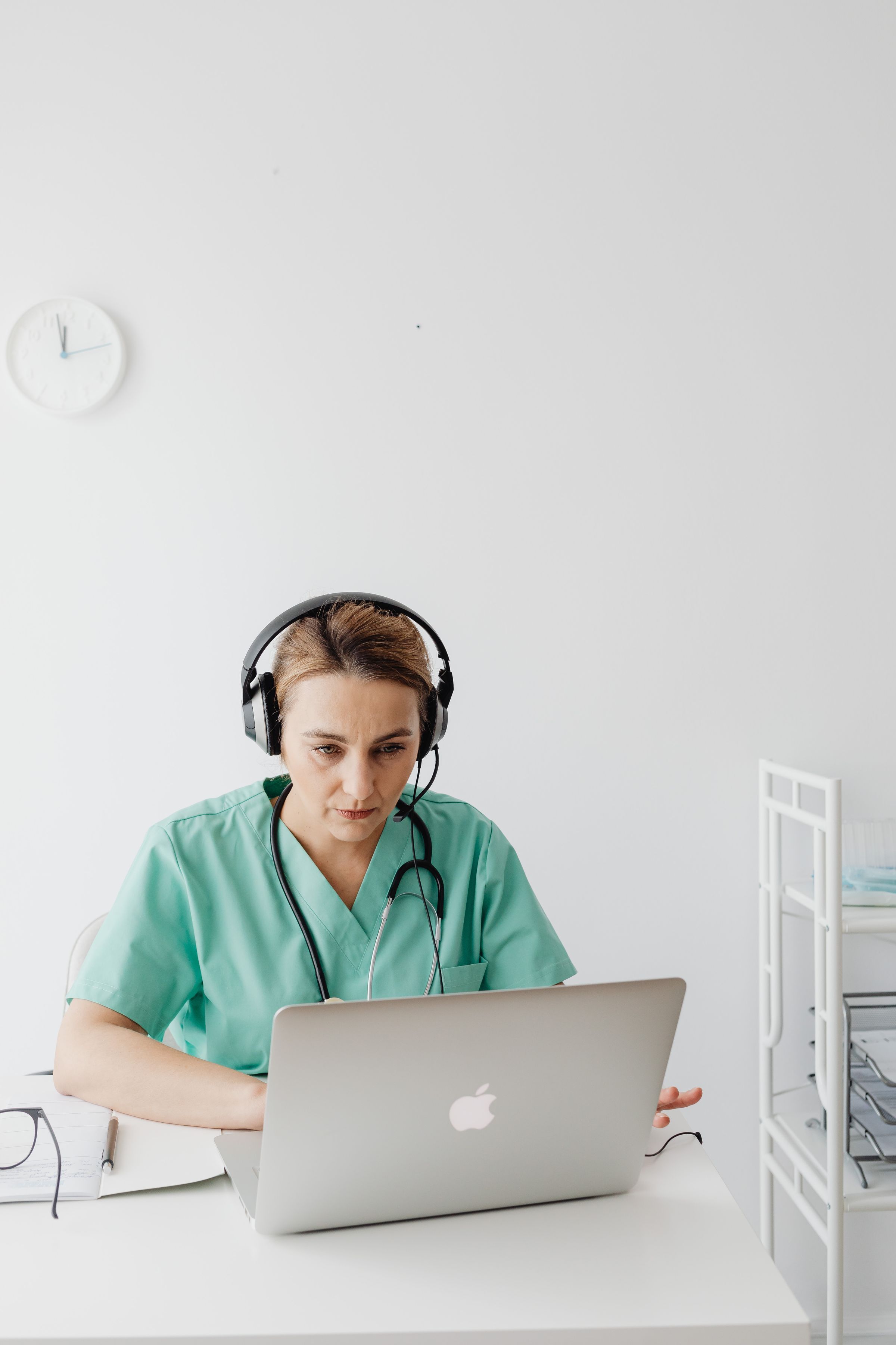 A woman in green scrubs using a laptop and headset.