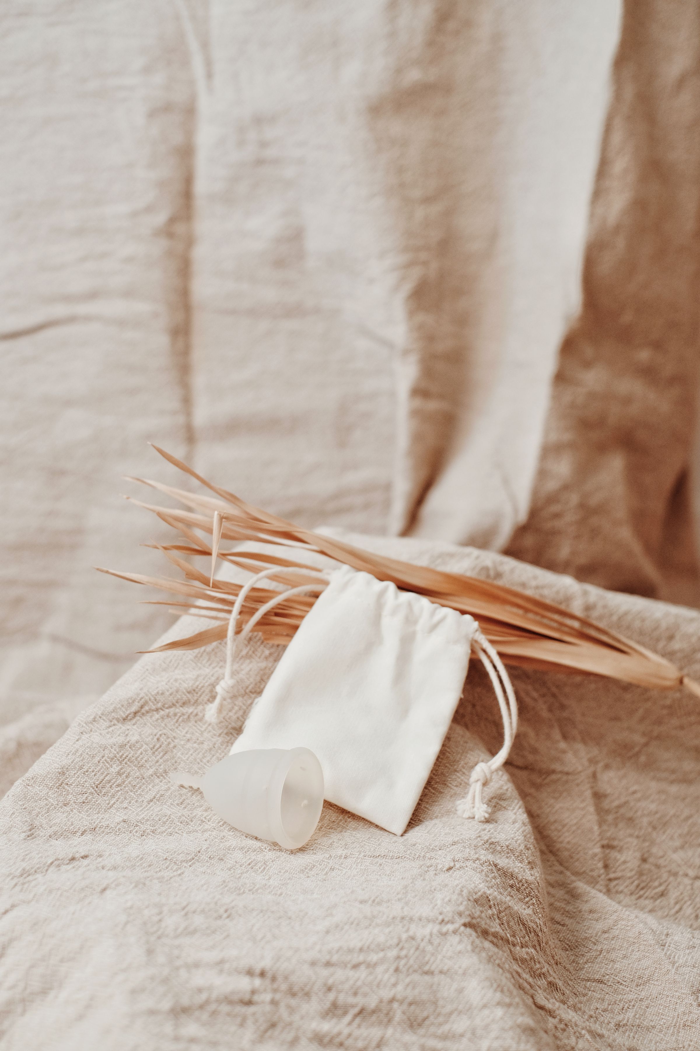 A menstrual cup beside a fabric pouch on a linen surface.