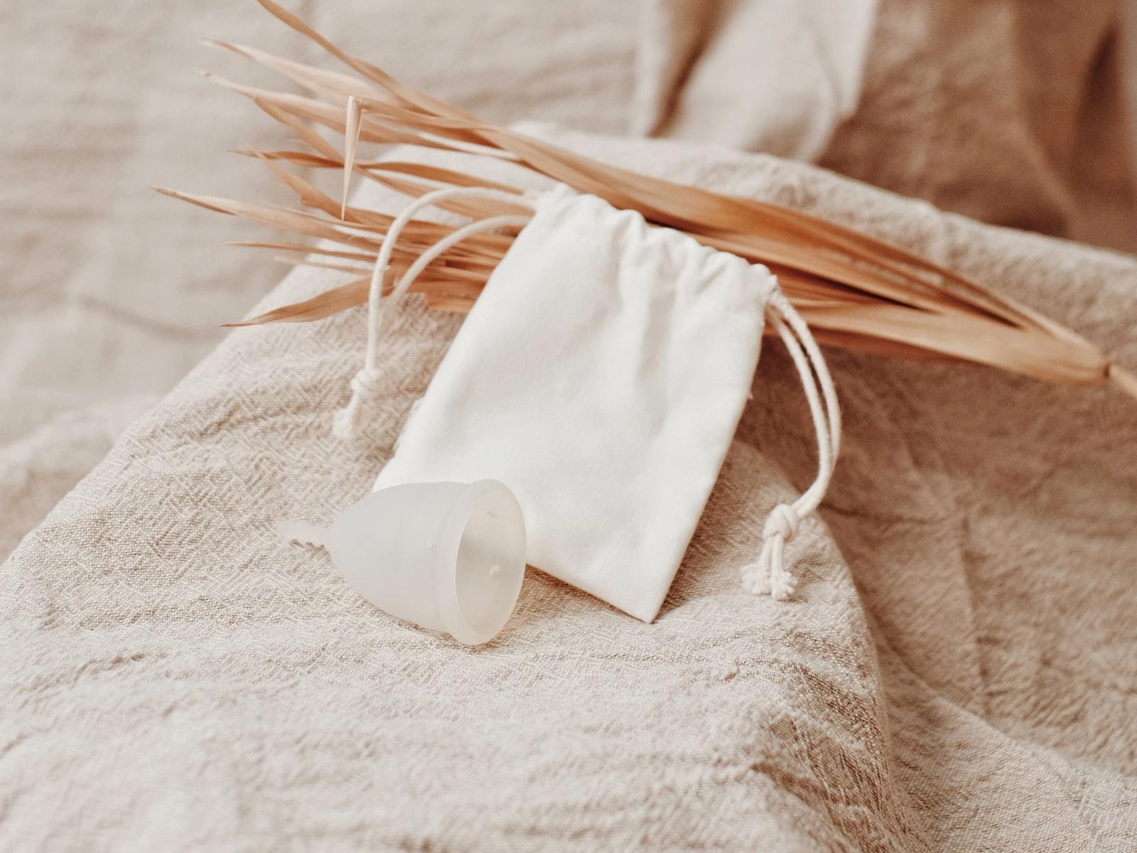 A menstrual cup beside a fabric pouch on a linen surface.