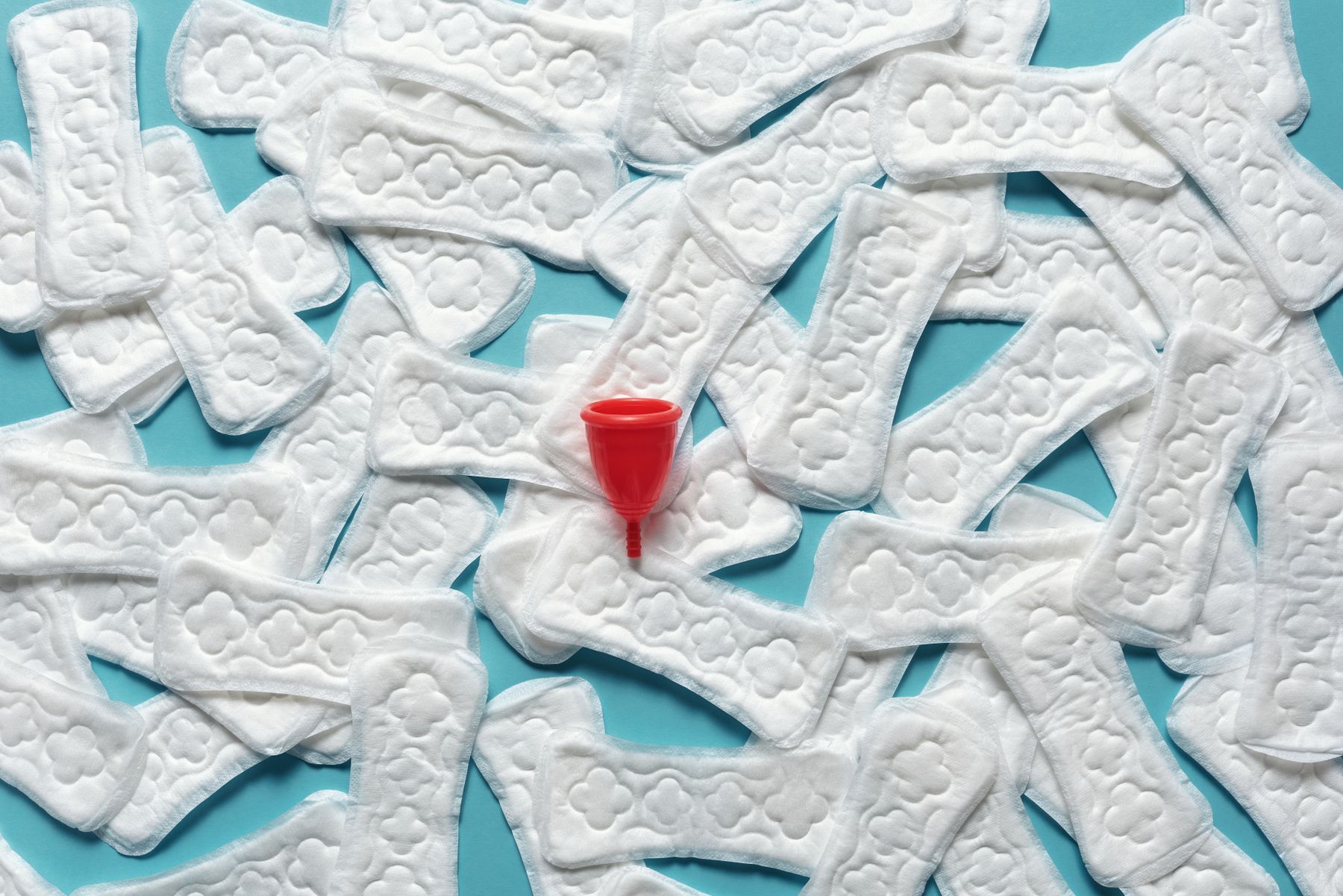 A menstrual cup surrounded by wrapped sanitary pads.