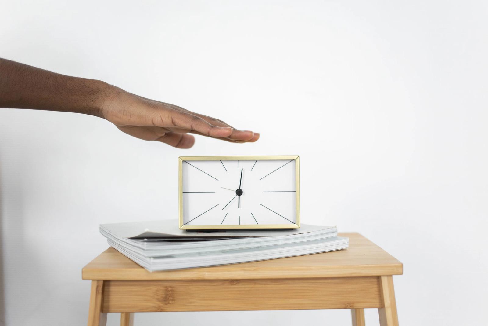 A hand touching an analog alarm clock on a table.
