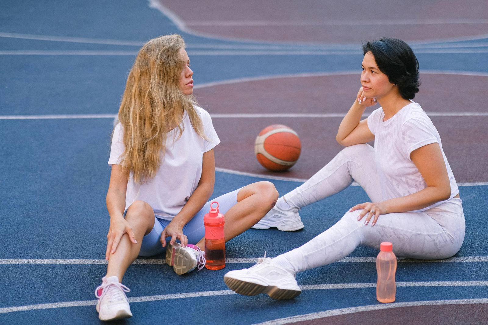 Two women talking beside an outdoor sports court.