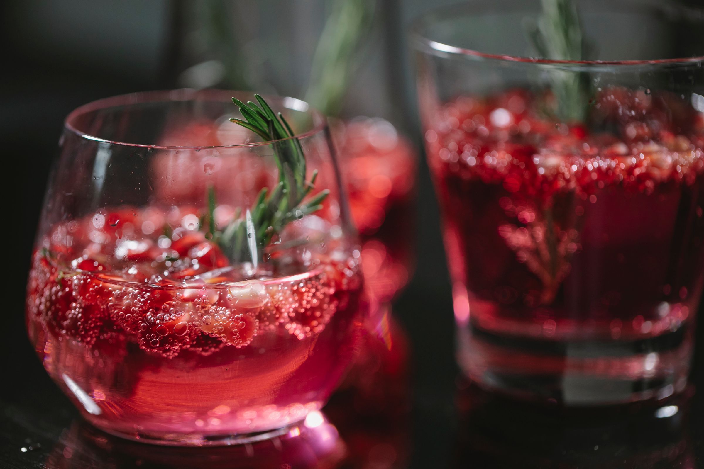 Red drinks with berries and rosemary in glasses.