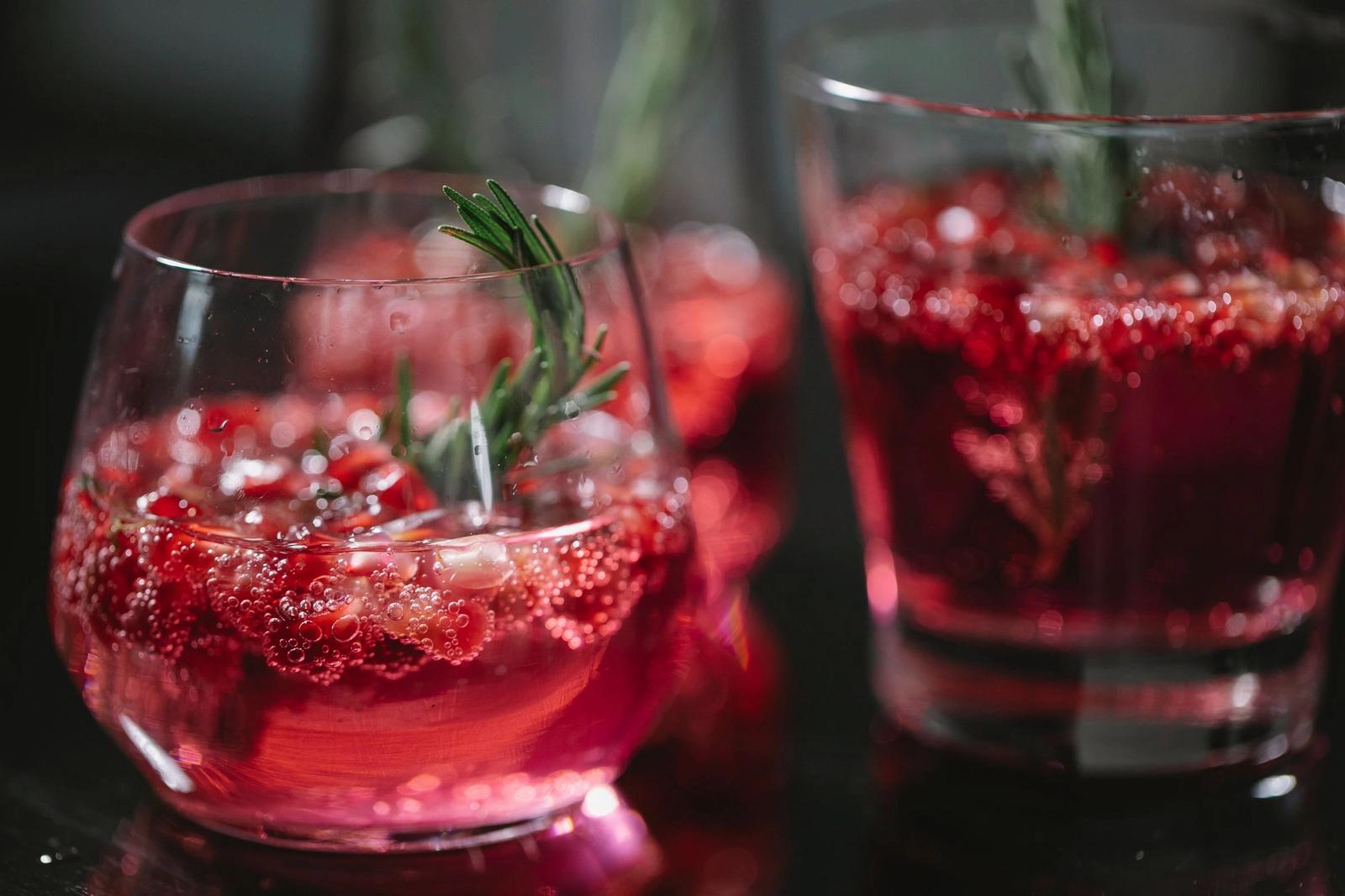 Red drinks with berries and rosemary in glasses.