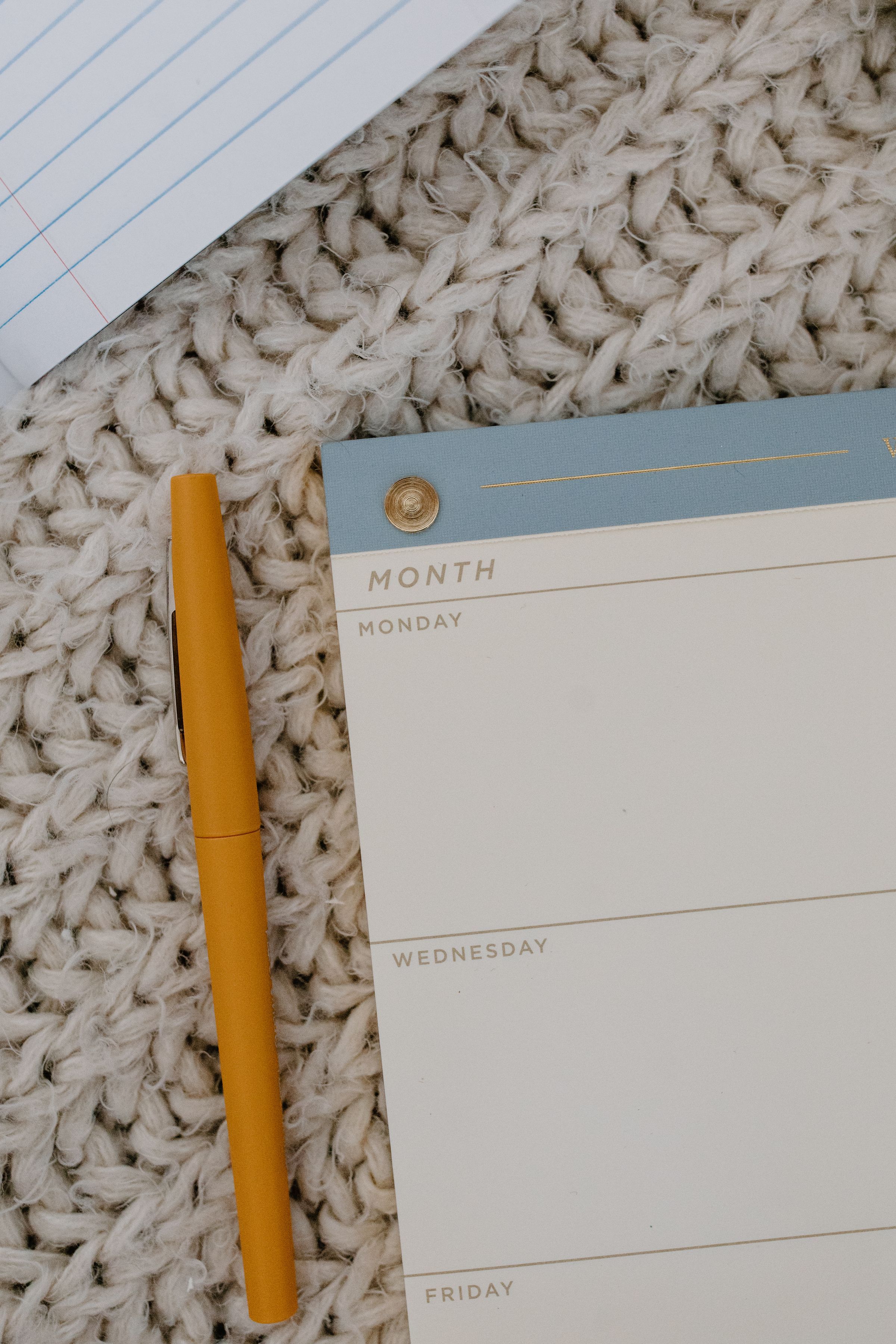 A pencil beside a weekly planner on a knitted surface.