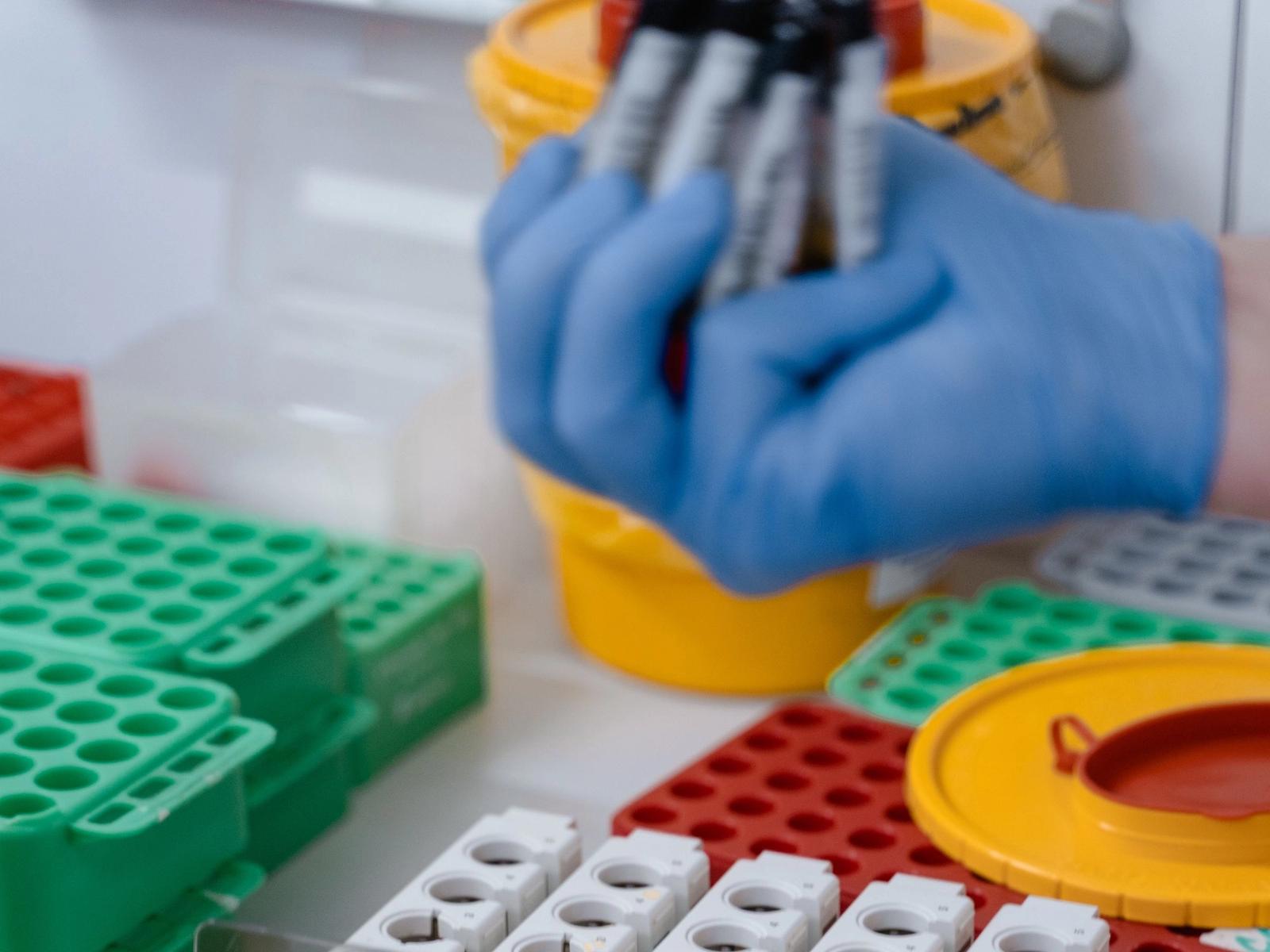 Gloved hands handling sample tubes in a laboratory.