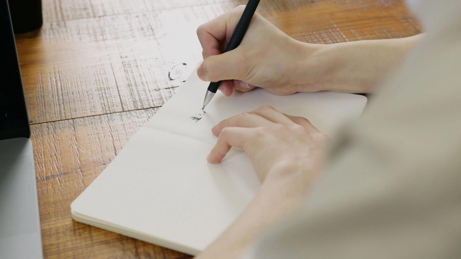 Hands writing notes in a notebook on a table.