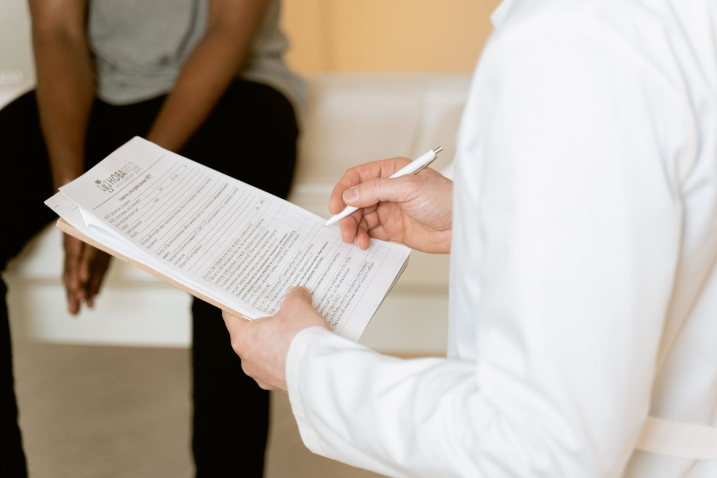 Hands holding a clipboard and pen during a consultation.