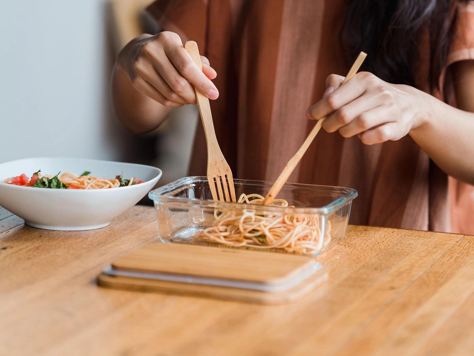 Hands serving pasta at a table.