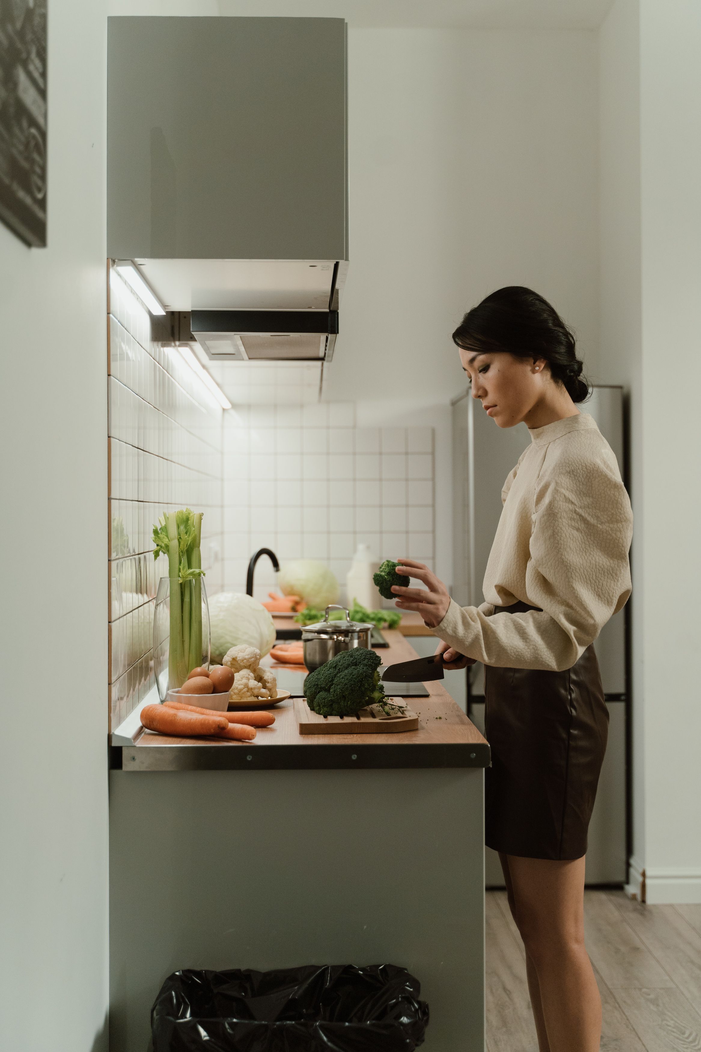 A woman preparing broccoli and other vegetables in a kitchen.