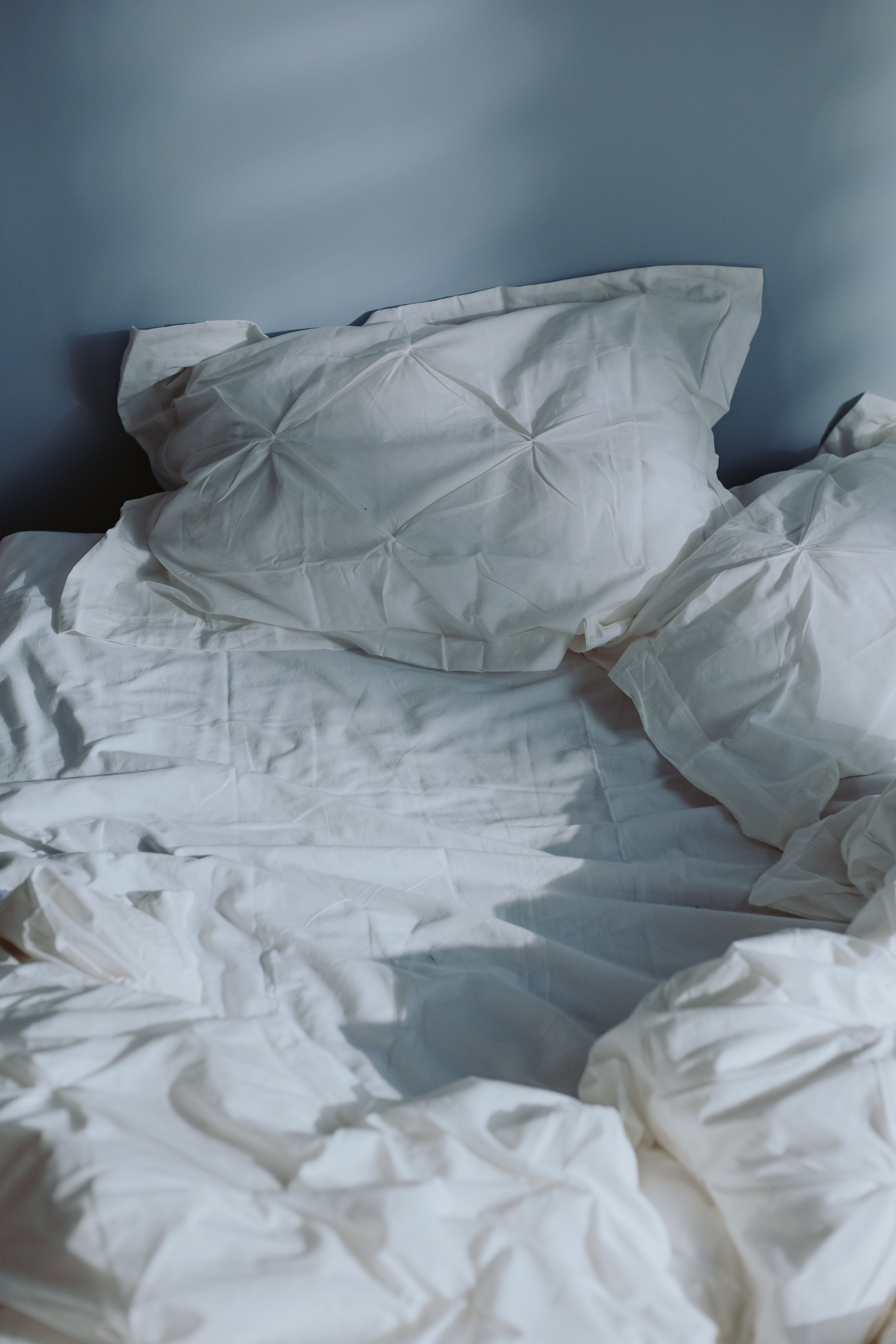 An unmade bed with white pillows and sheets.