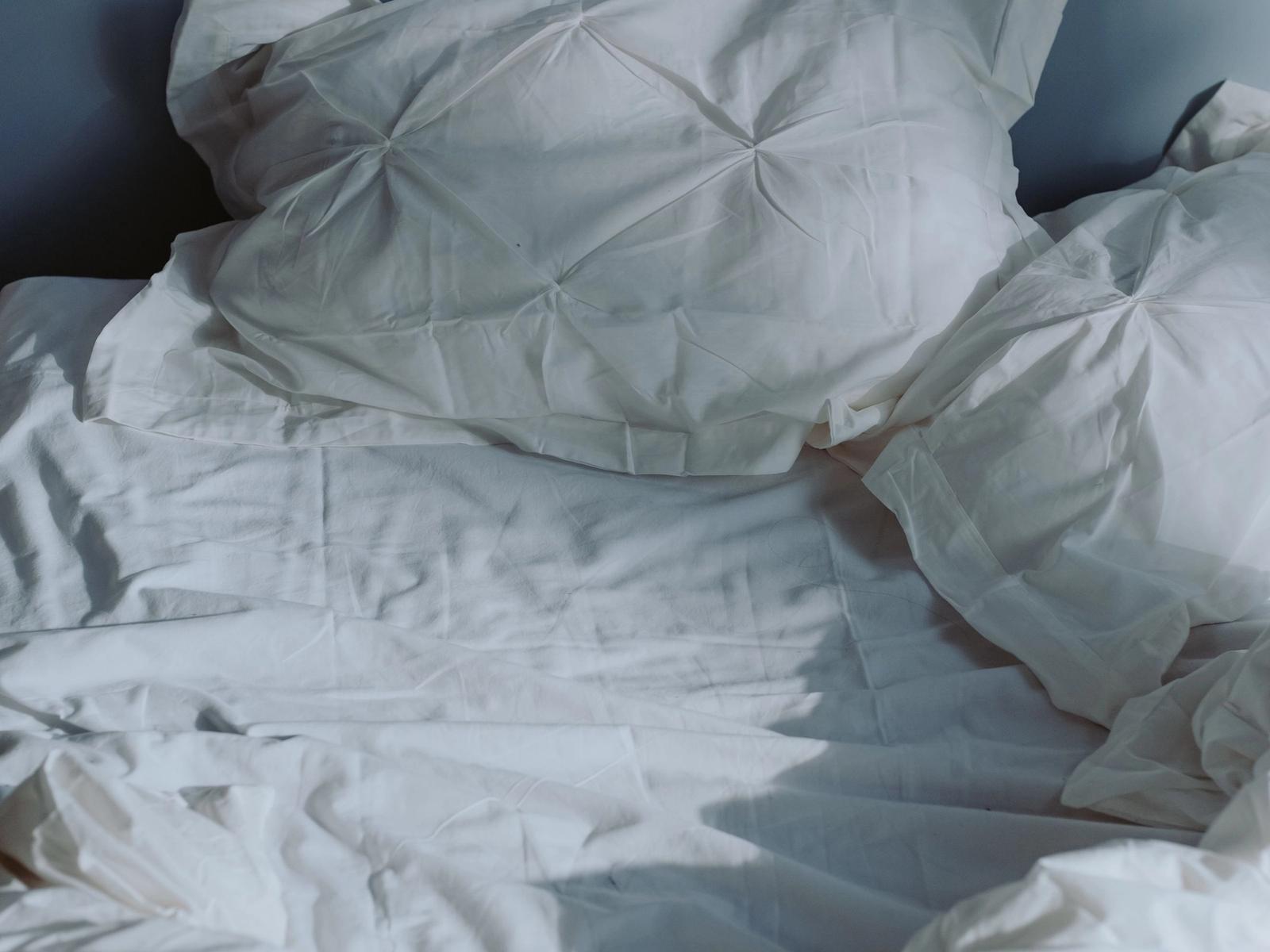 An unmade bed with white pillows and sheets.