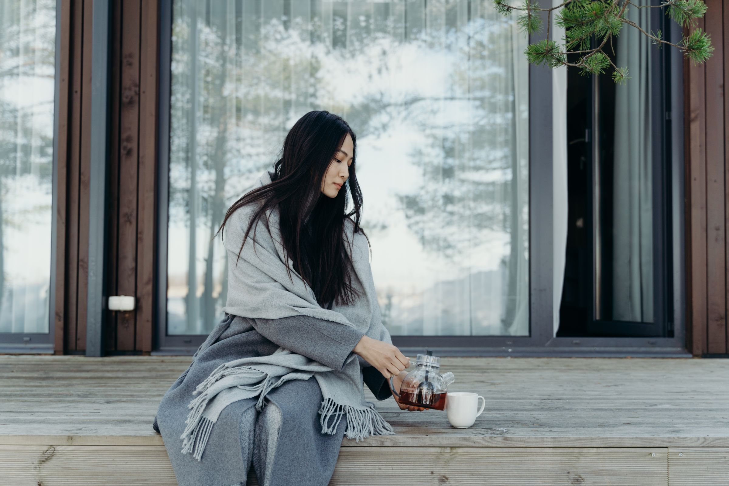 A woman wrapped in a blanket pouring tea outdoors.