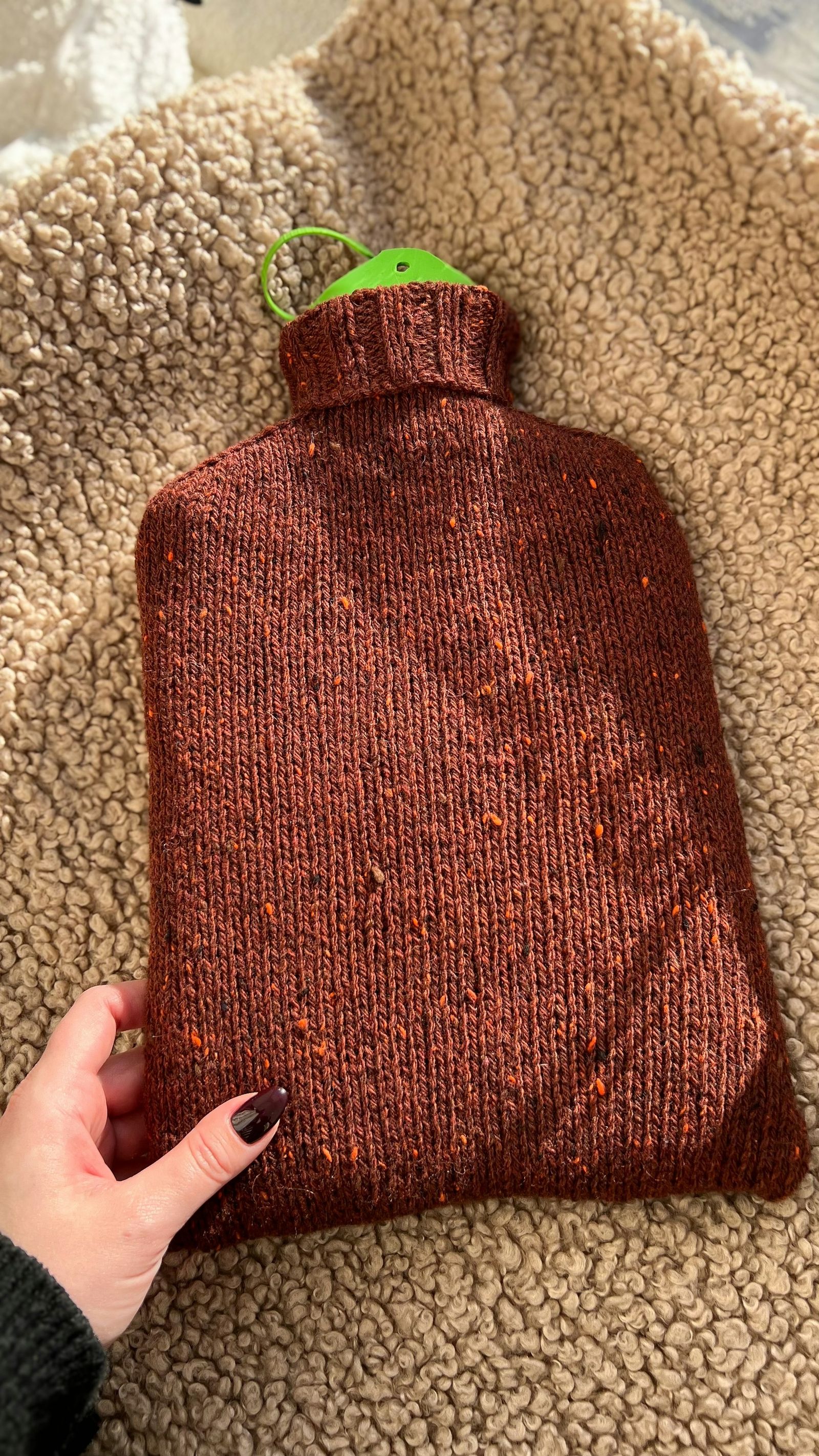 A knitted hot-water bottle with a green stopper.