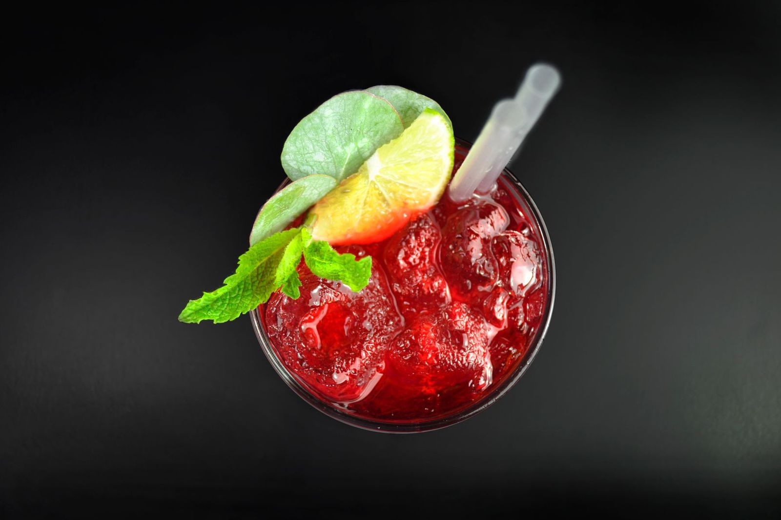A red drink with ice and a green garnish.