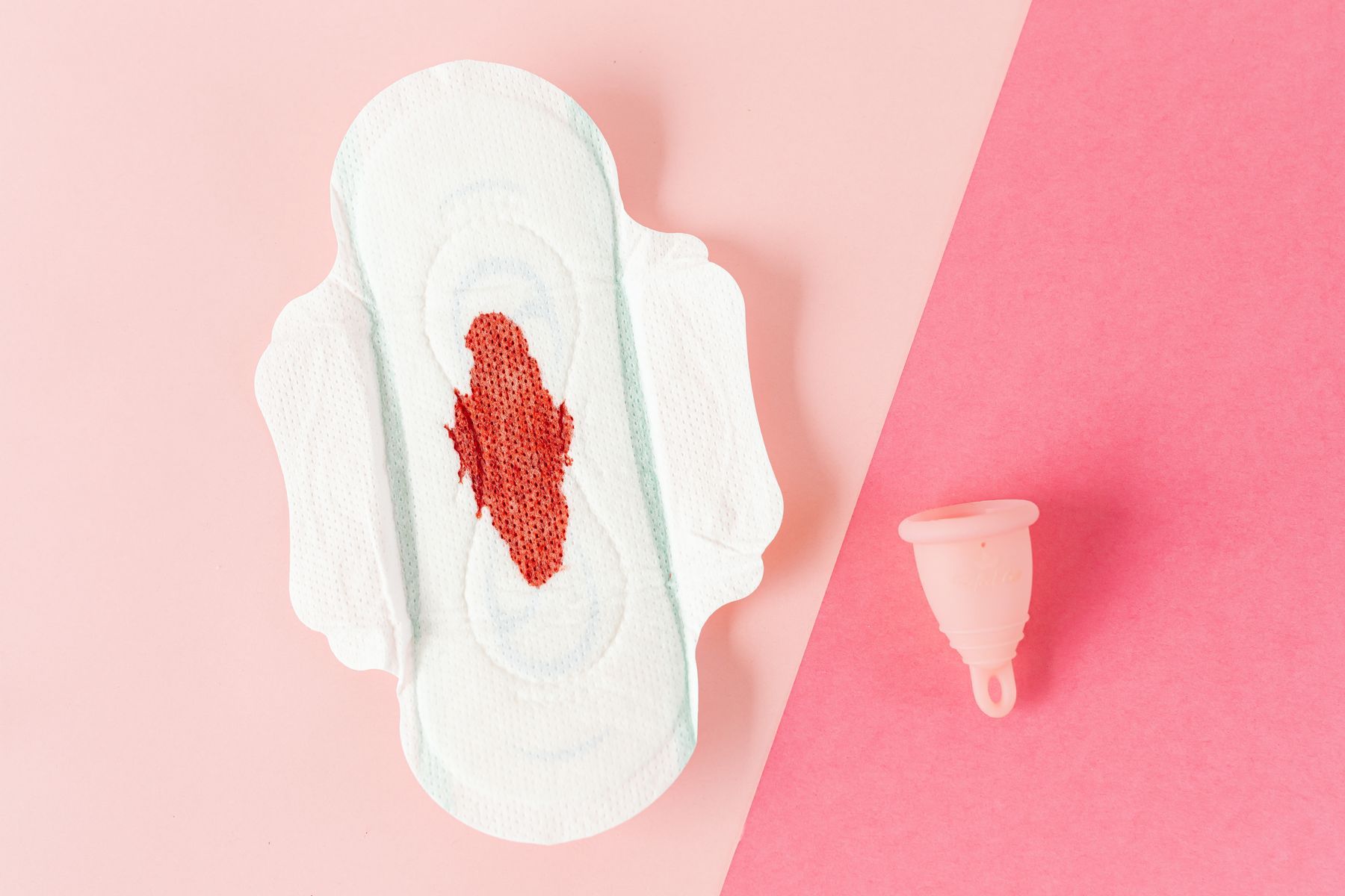 A sanitary pad with a red stain beside a menstrual cup.