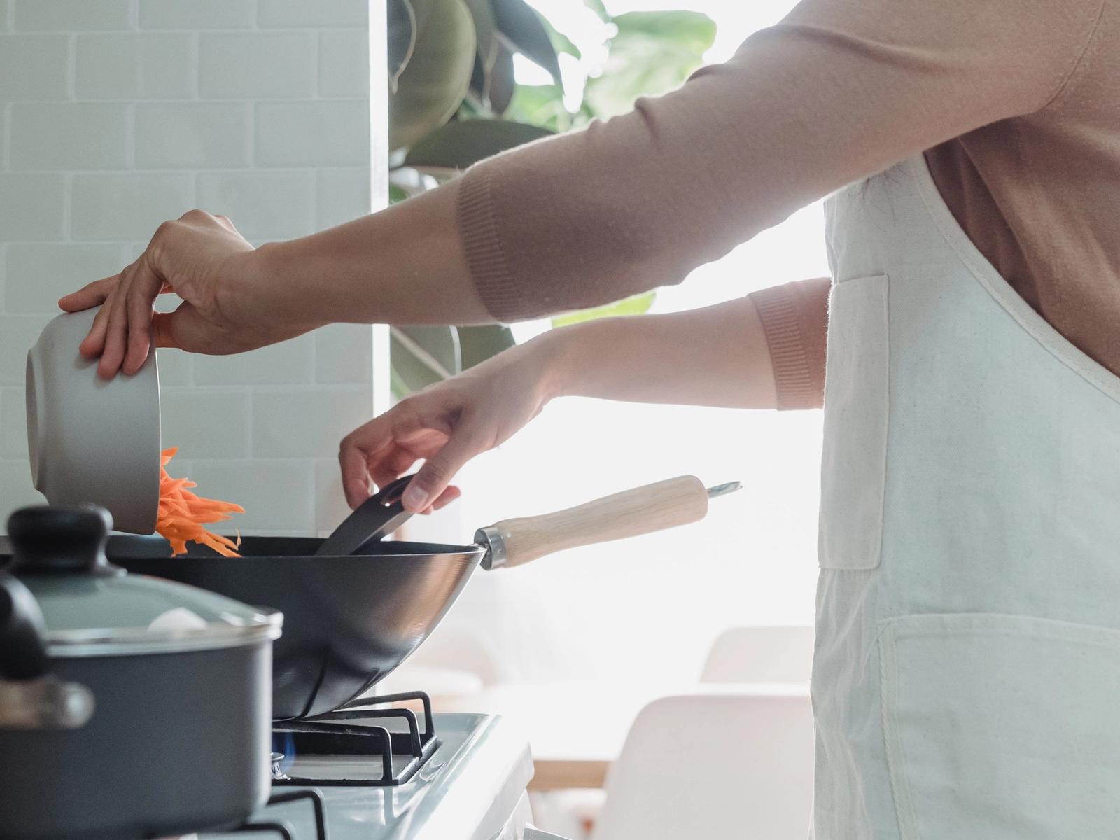 Hands stirring food in a pan at a cooker.