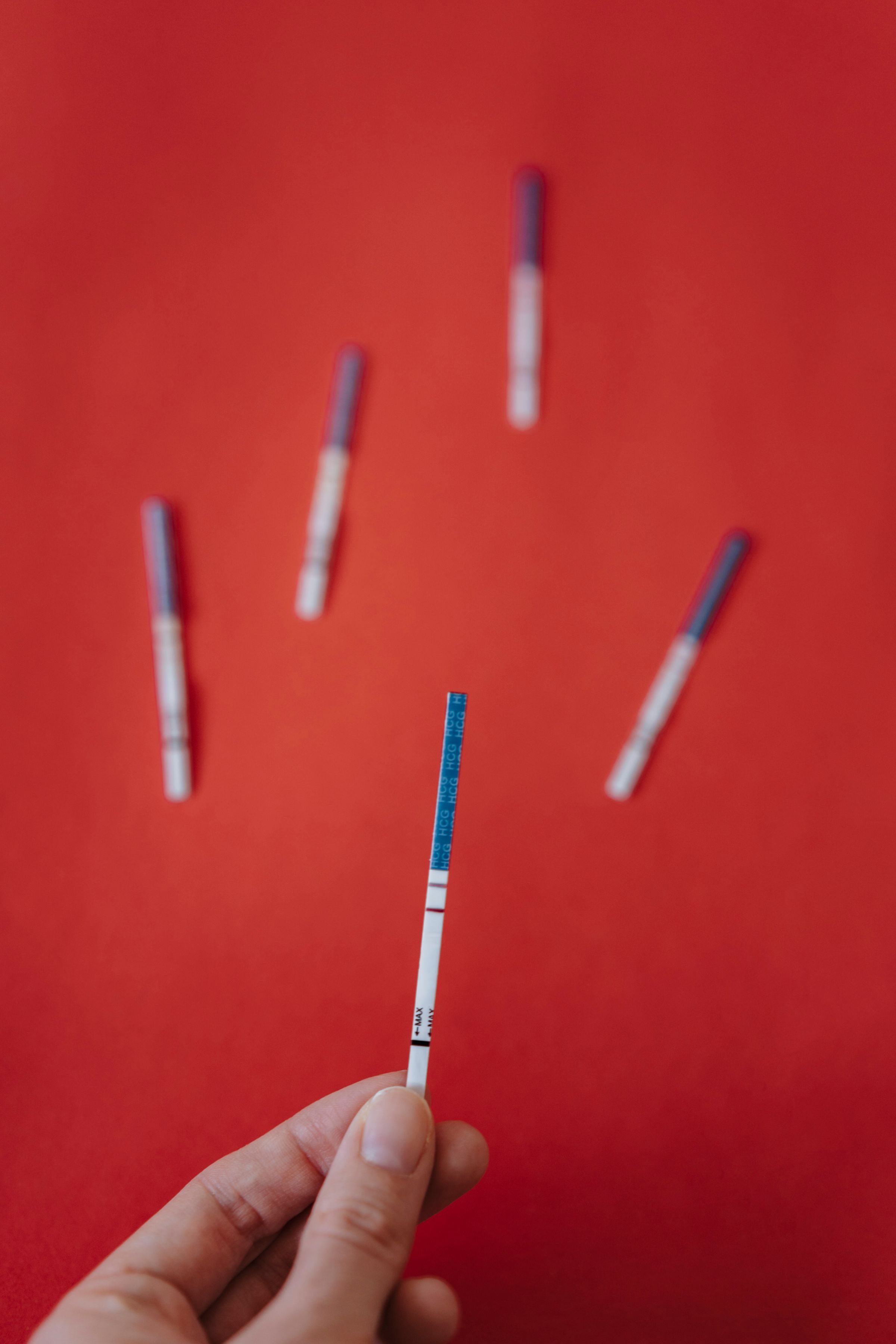 A hand holding a pregnancy test strip against a red background.