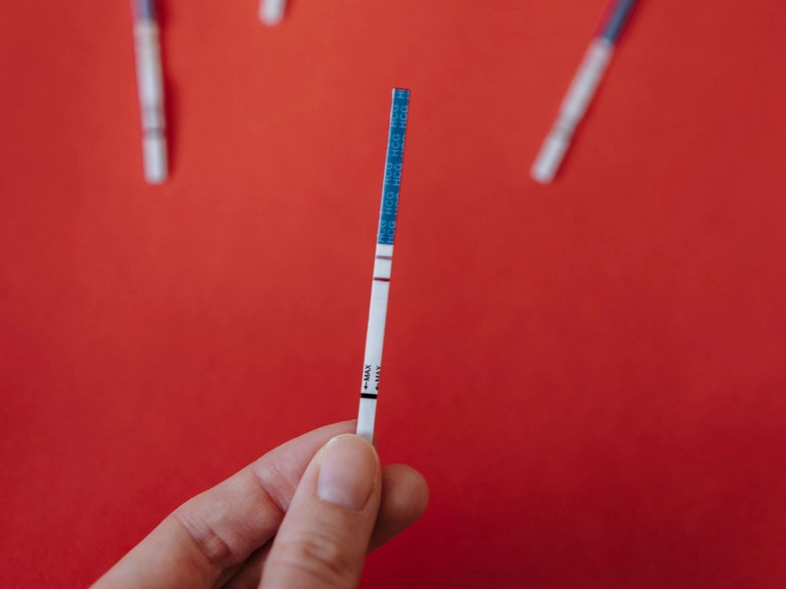 A hand holding a pregnancy test strip against a red background.