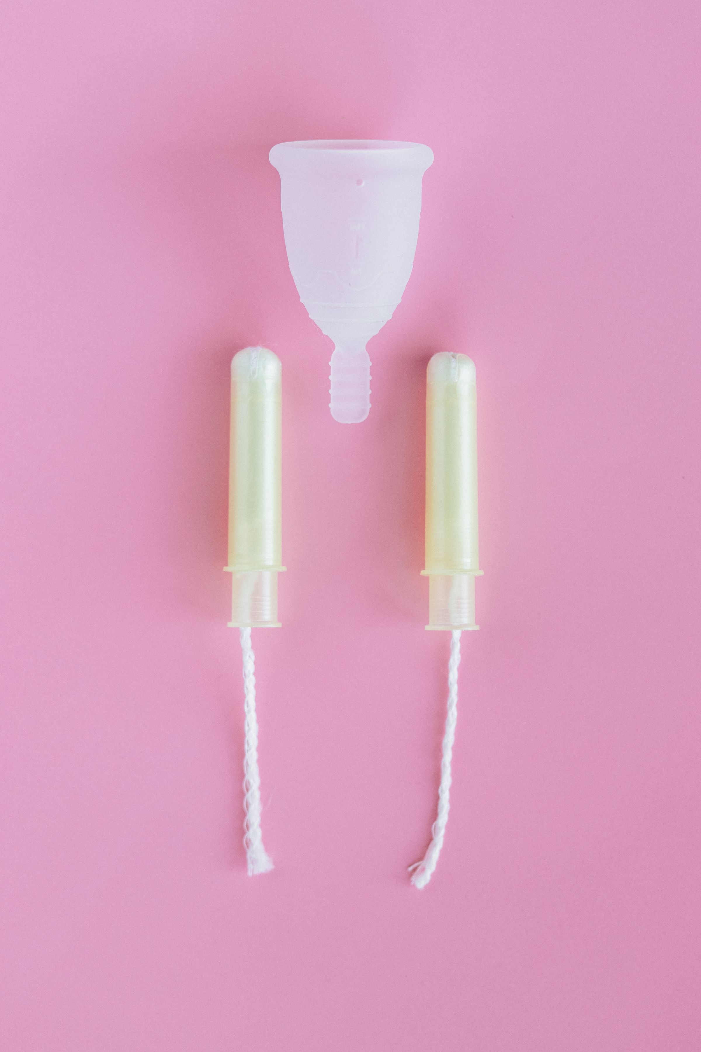 A menstrual cup and two tampons on a pink background.