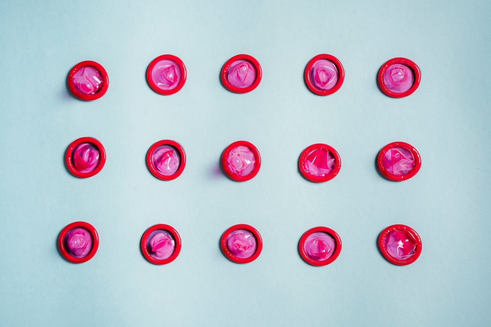 Pink condoms arranged on a blue surface.