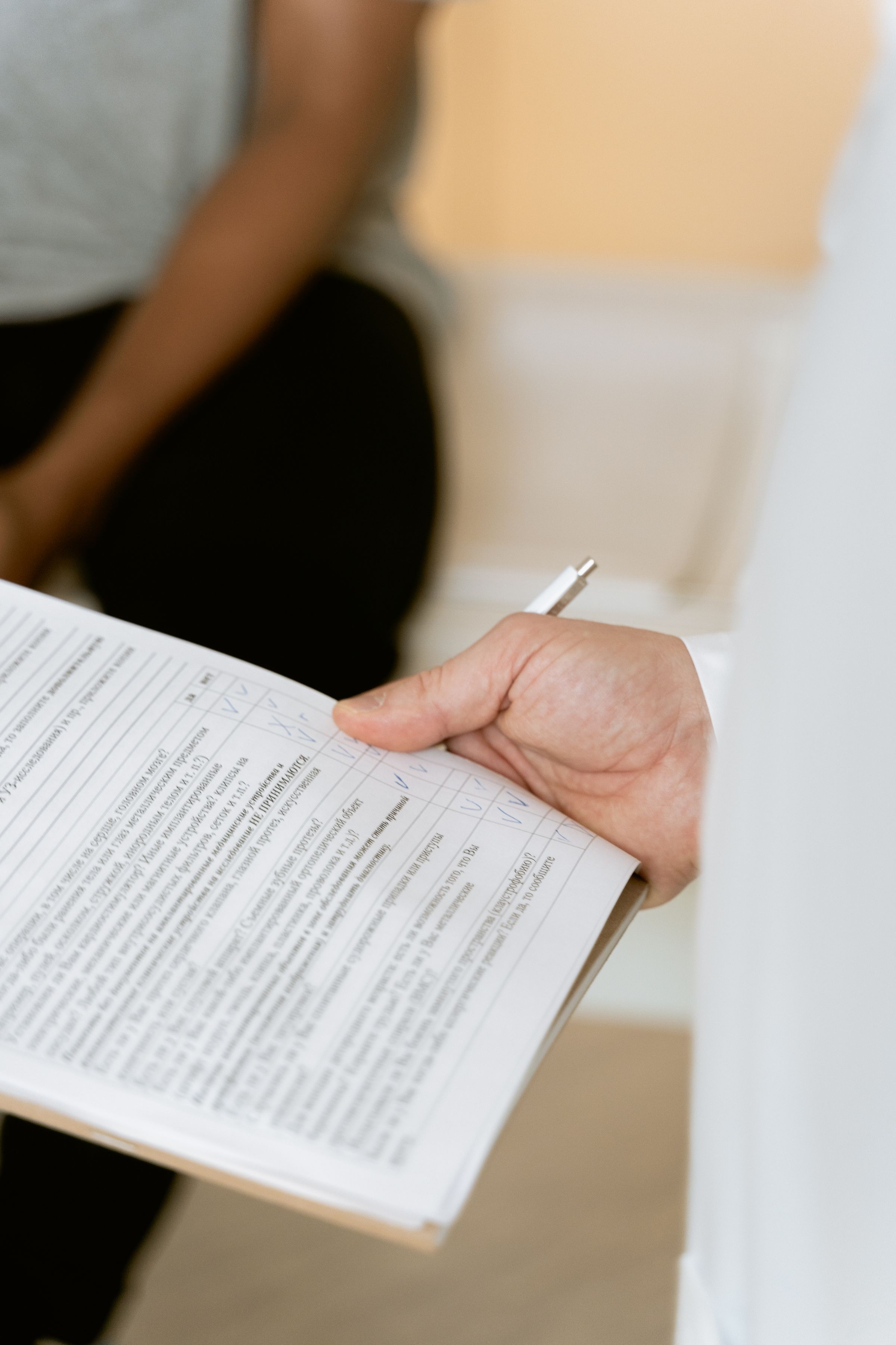 A person in a white coat holding a clipboard during a consultation.