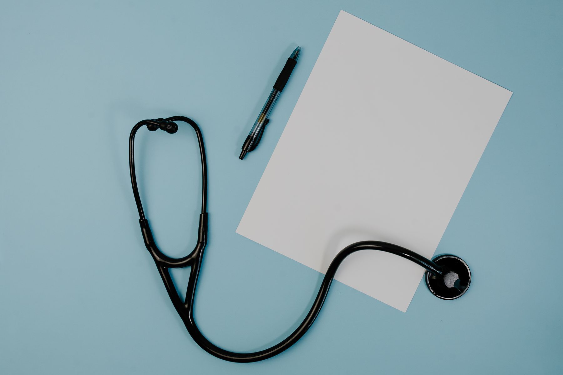 A stethoscope and pen beside a blank notepad.