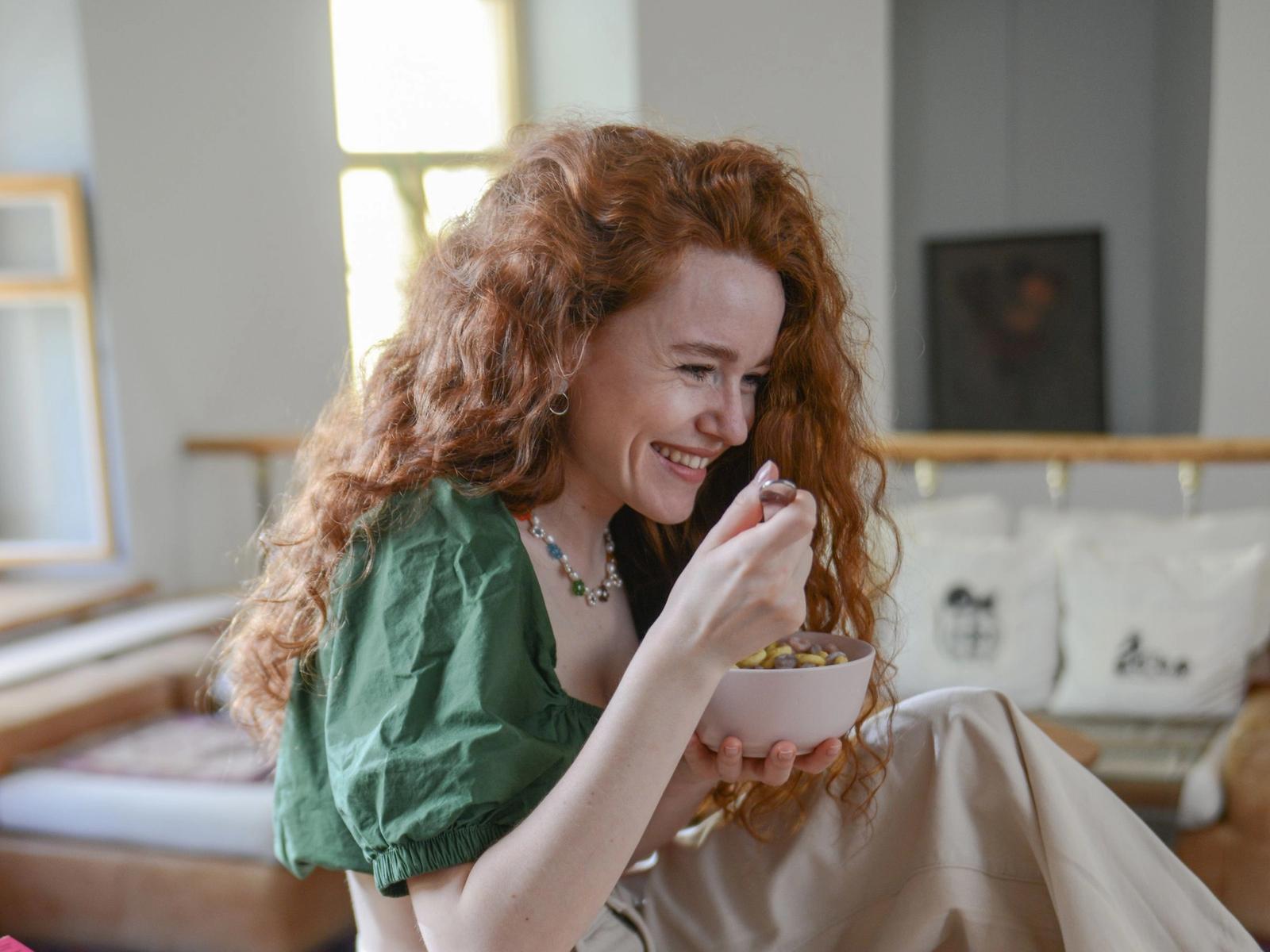 A woman eating from a bowl at a breakfast table.