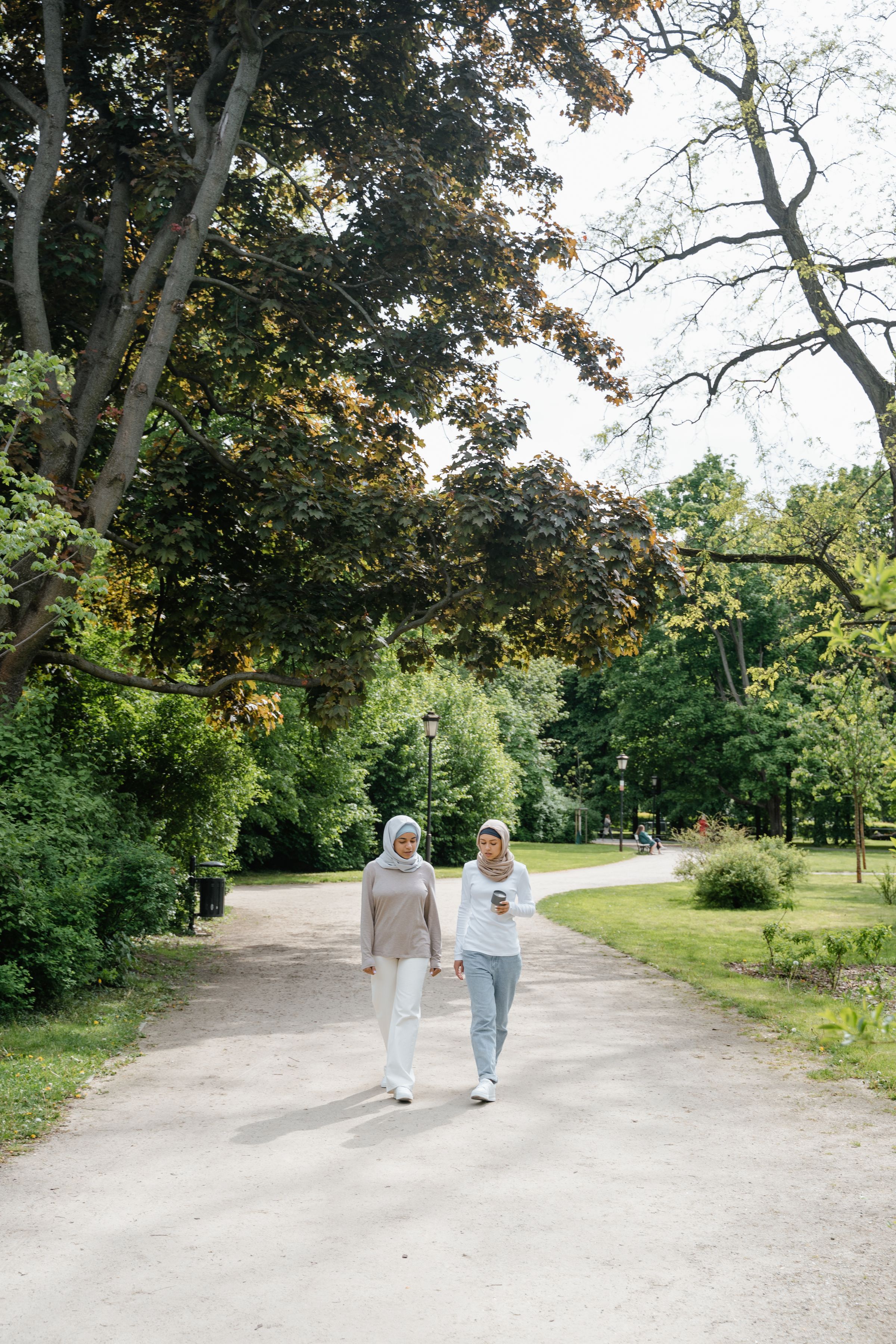 Two women walking along a path in a green park.
