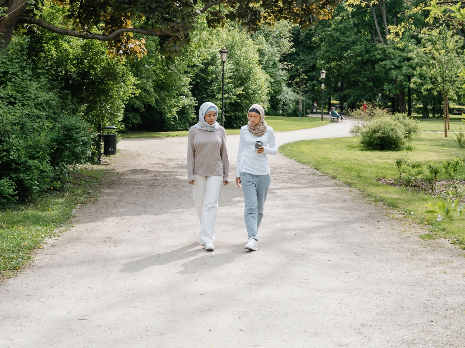 Two women walking along a path in a green park.