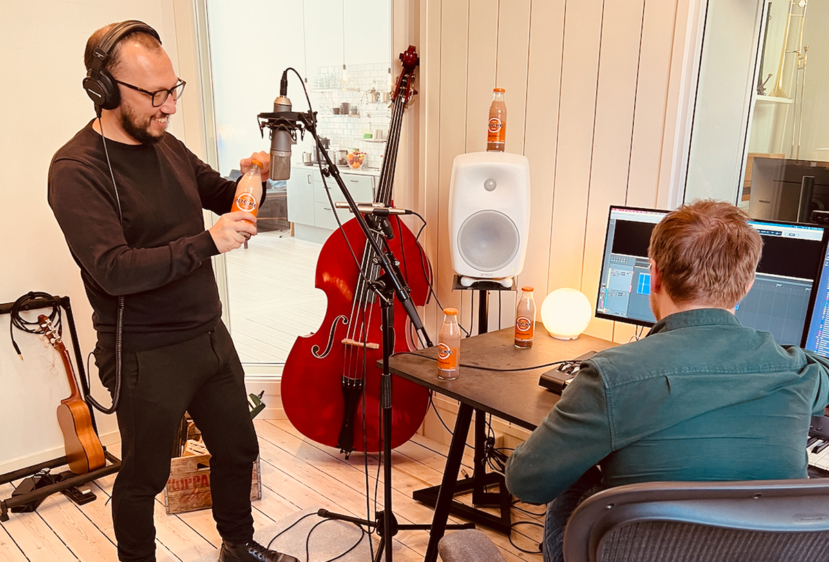 Two men holding a professional microphone close to a Pucko chocolate drink bottle during an audio recording session.