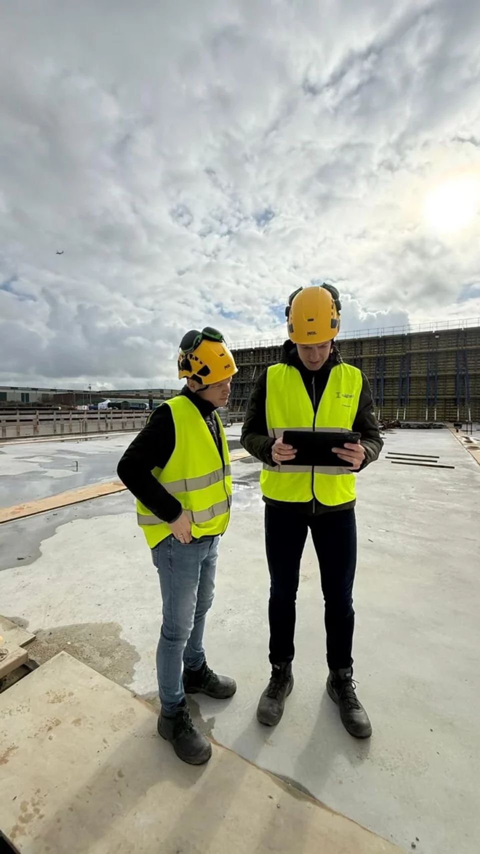 Twee mensen bouwhelmen en vestjes op een bouwgrond