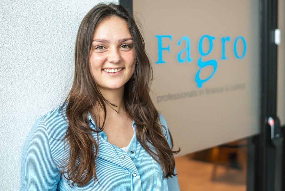 Vrouw met lang bruin haar, kijkt glimlachend de camera in
