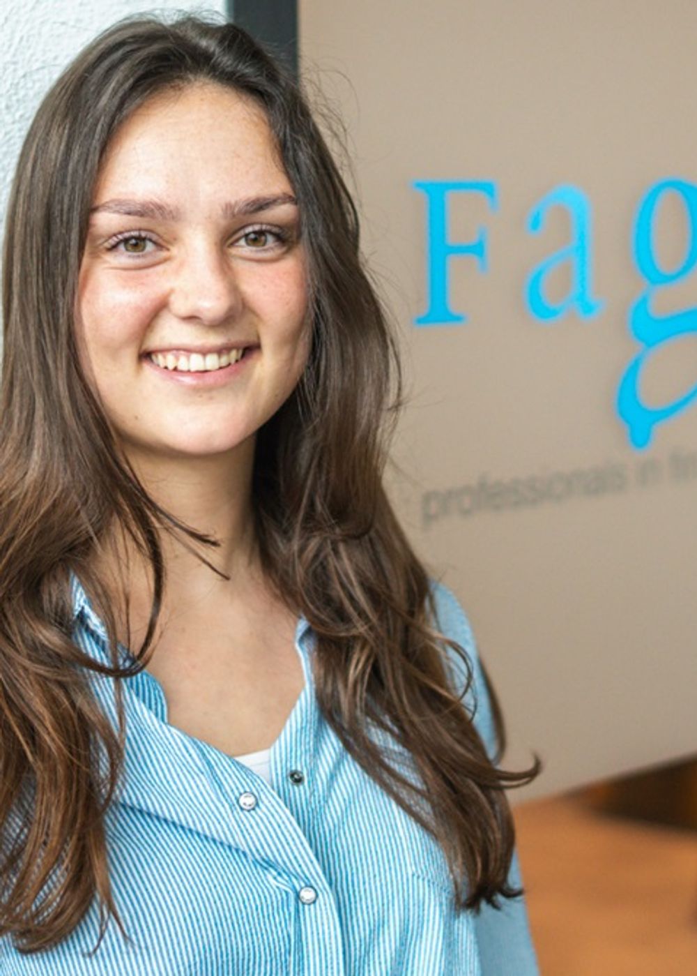 Vrouw met lang bruin haar, kijkt glimlachend de camera in