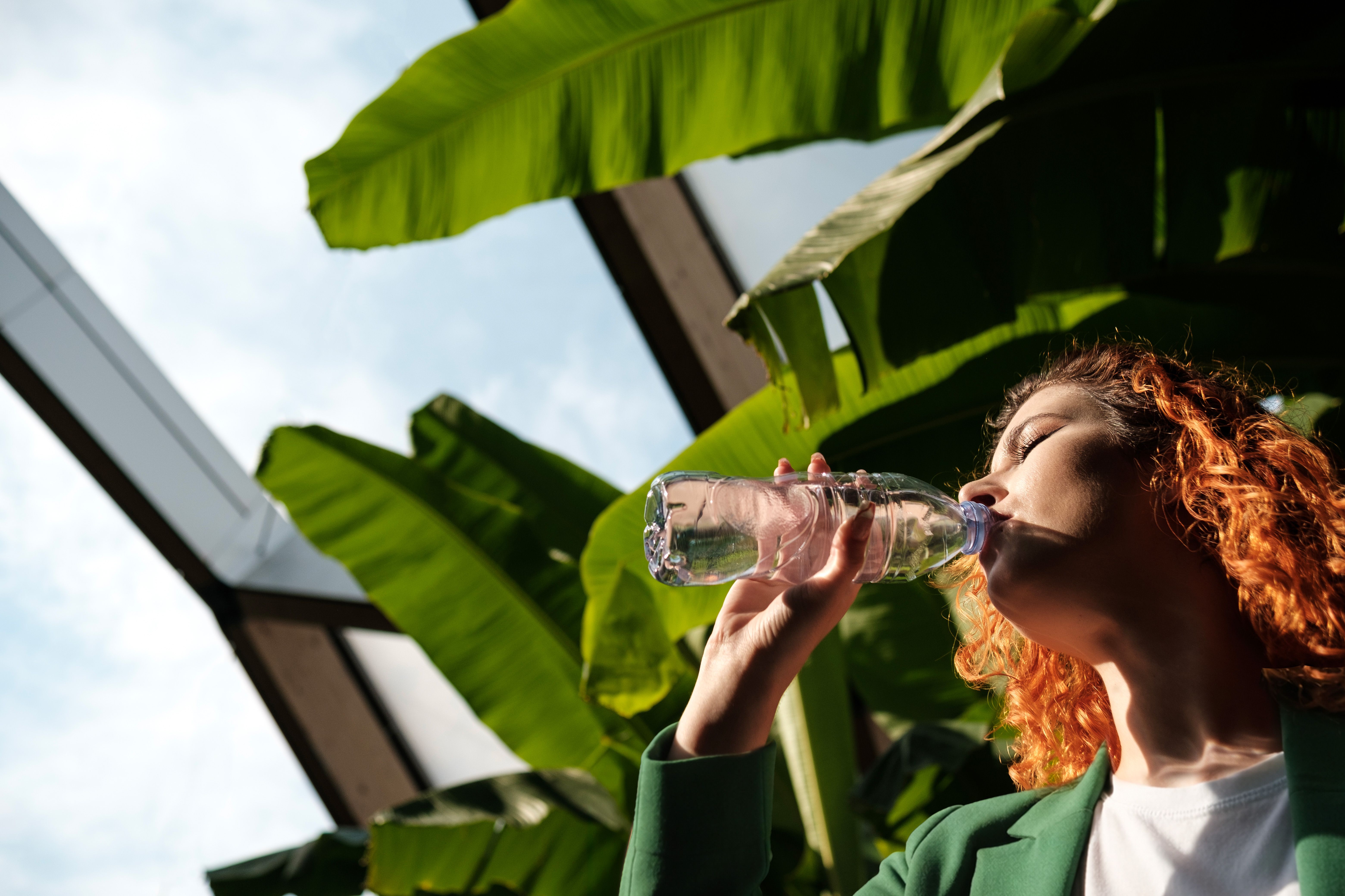 Vrouw voor bananenplant die een slok neemt uit een fles water
