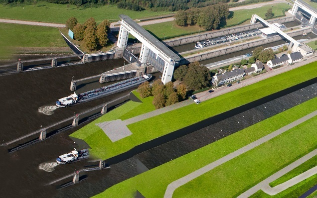 Luchtfoto toont monumentale Prinses Beatrixsluis met witte sluisdeuren, binnenvaartschepen in de sluiskolk en groen landschap rondom het Lekkanaal"