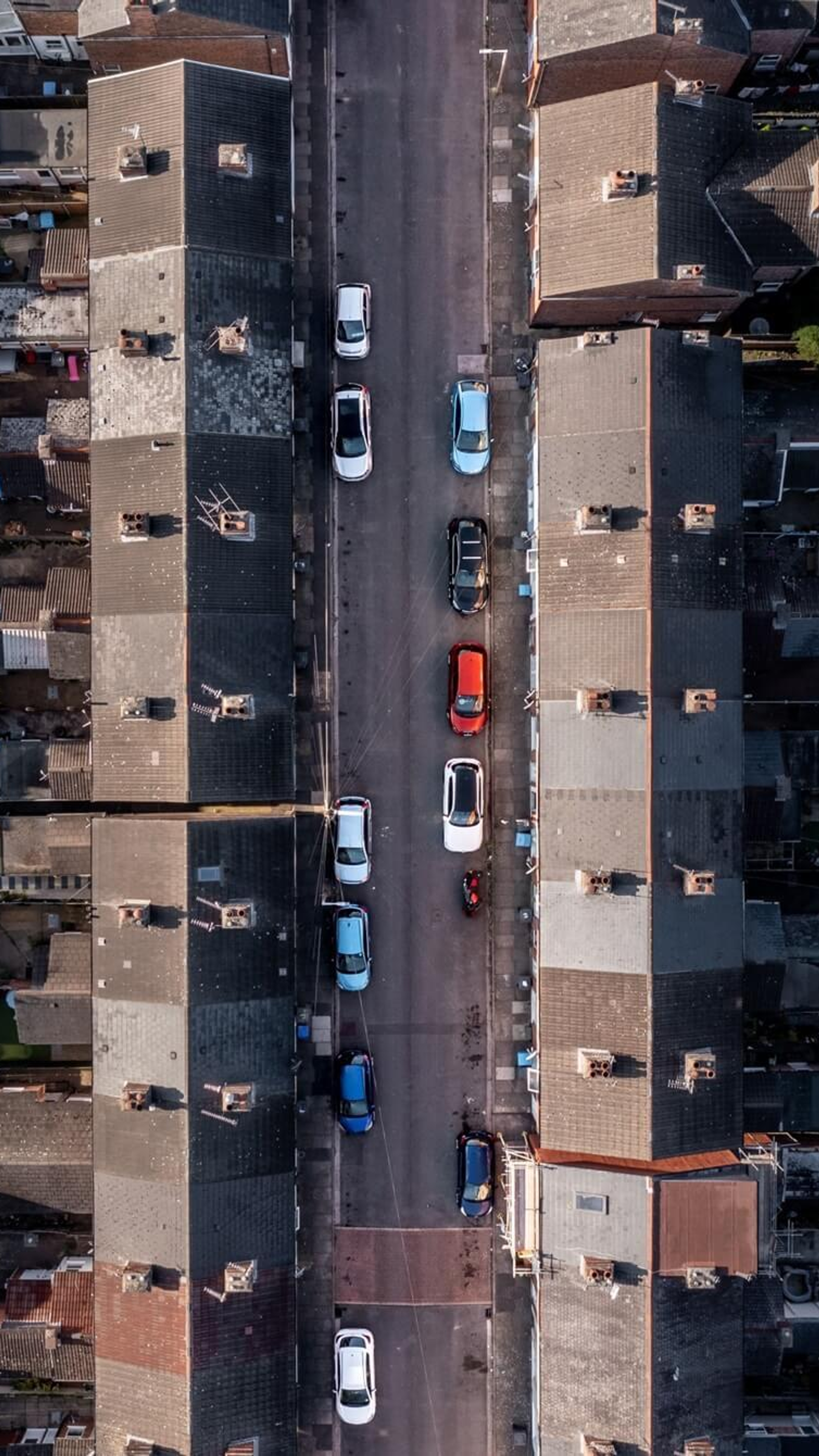 Luchtfoto van een smalle straat met rijen aaneengeschakelde huizen en geparkeerde auto's, in een dichtbebouwde stedelijke wijk.