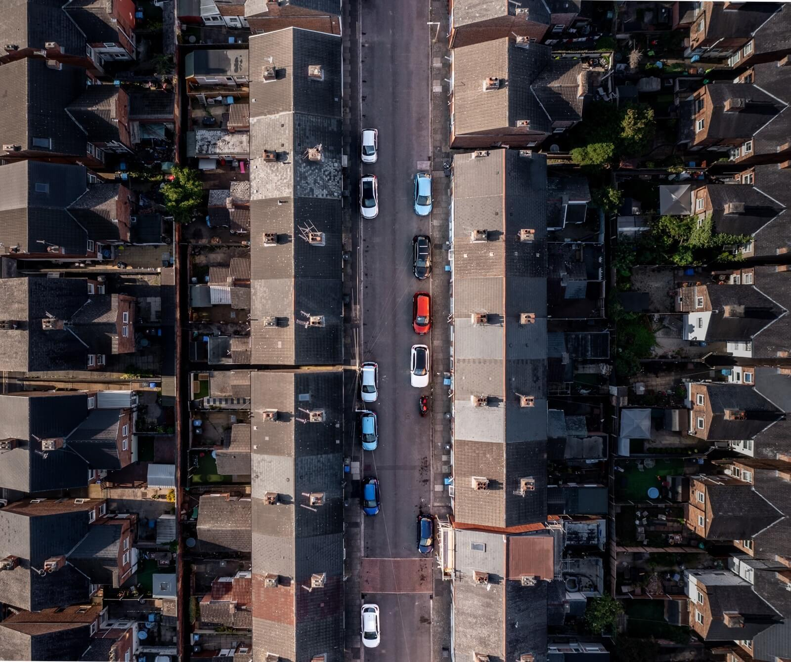 Luchtfoto van een smalle straat met rijen aaneengeschakelde huizen en geparkeerde auto's, in een dichtbebouwde stedelijke wijk.
