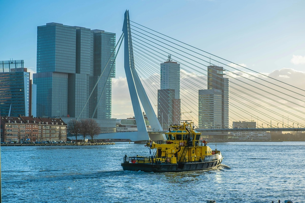 Gele havenboot vaart over de Maas in Rotterdam met op de achtergrond de Erasmusbrug en moderne hoogbouw aan de Kop van Zuid.